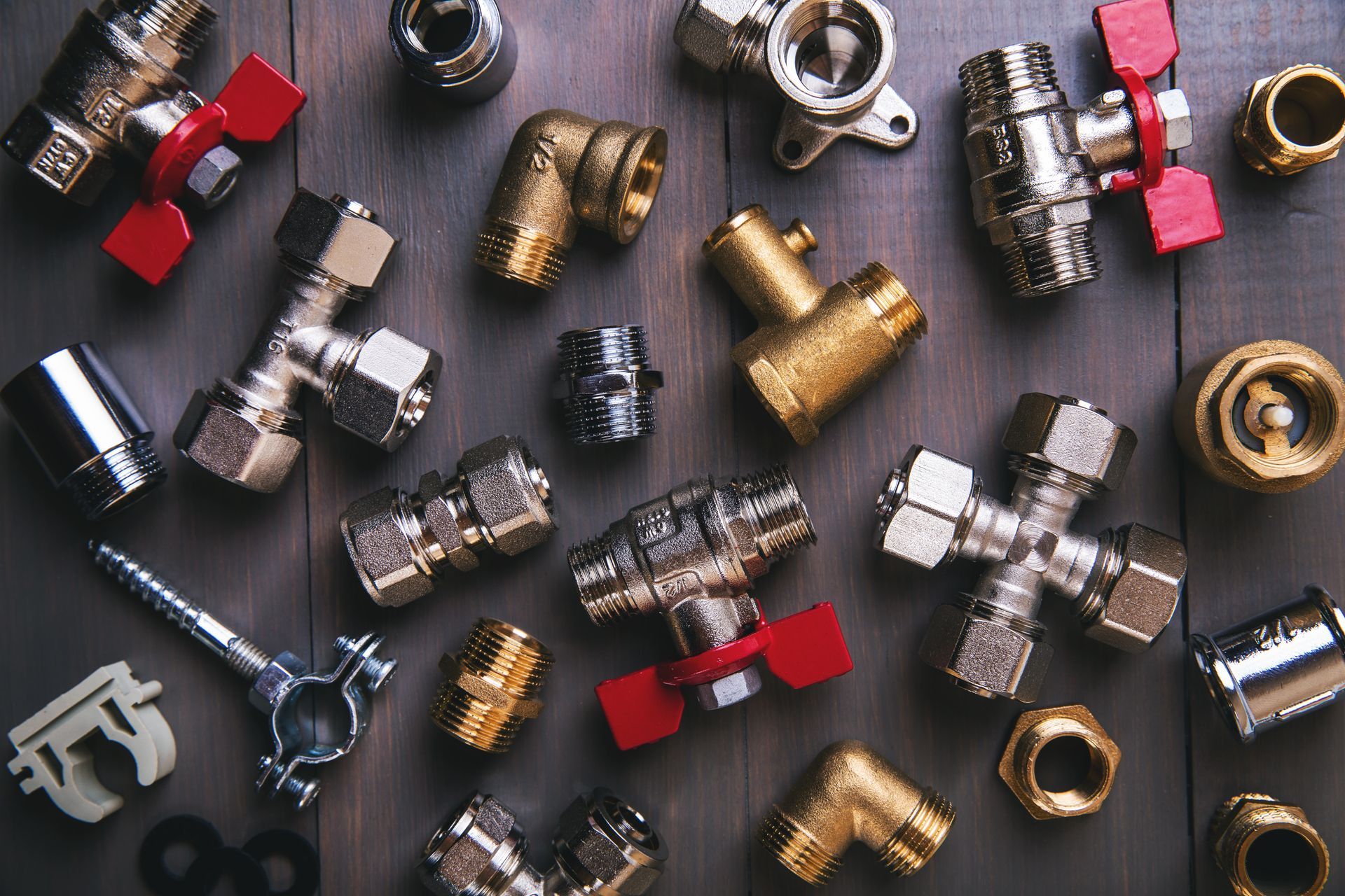 Assorted metal plumbing fittings and valves scattered on a dark surface, with red and silver pieces.