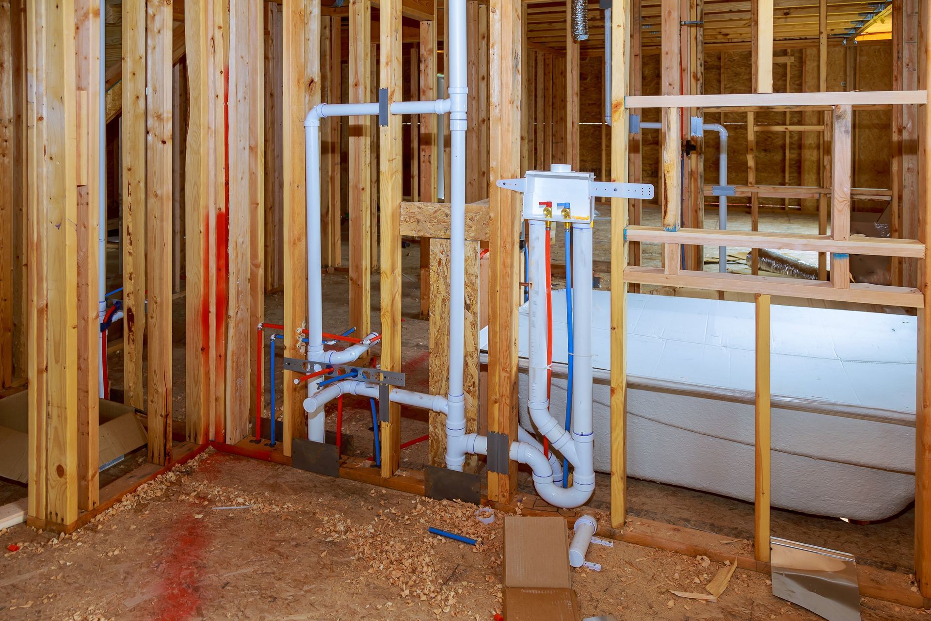 Framed bathroom plumbing with exposed pipes and a bathtub under construction