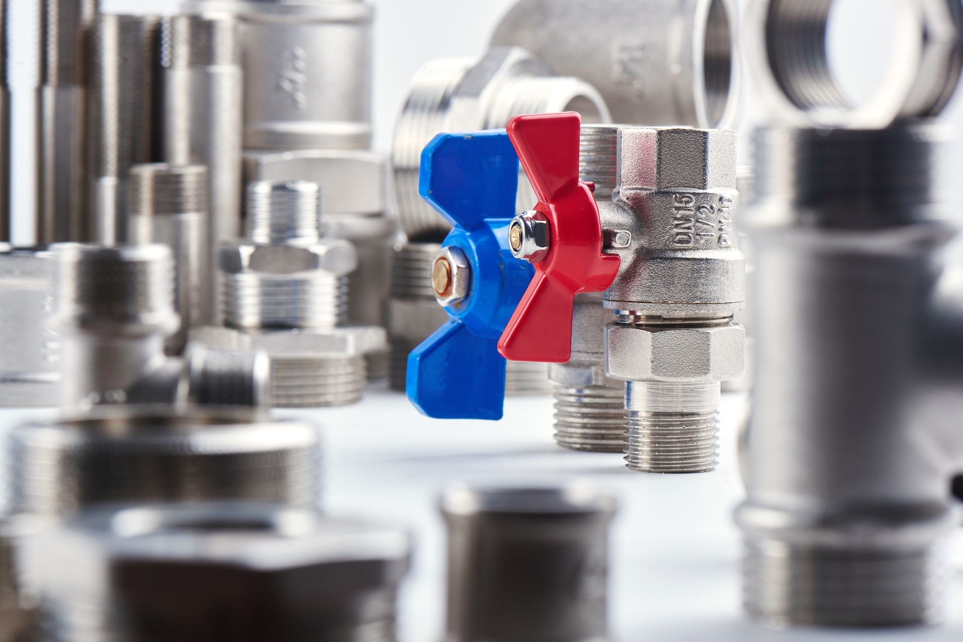 Blue and red valve handle among metal pipe fittings in a workshop-like setting