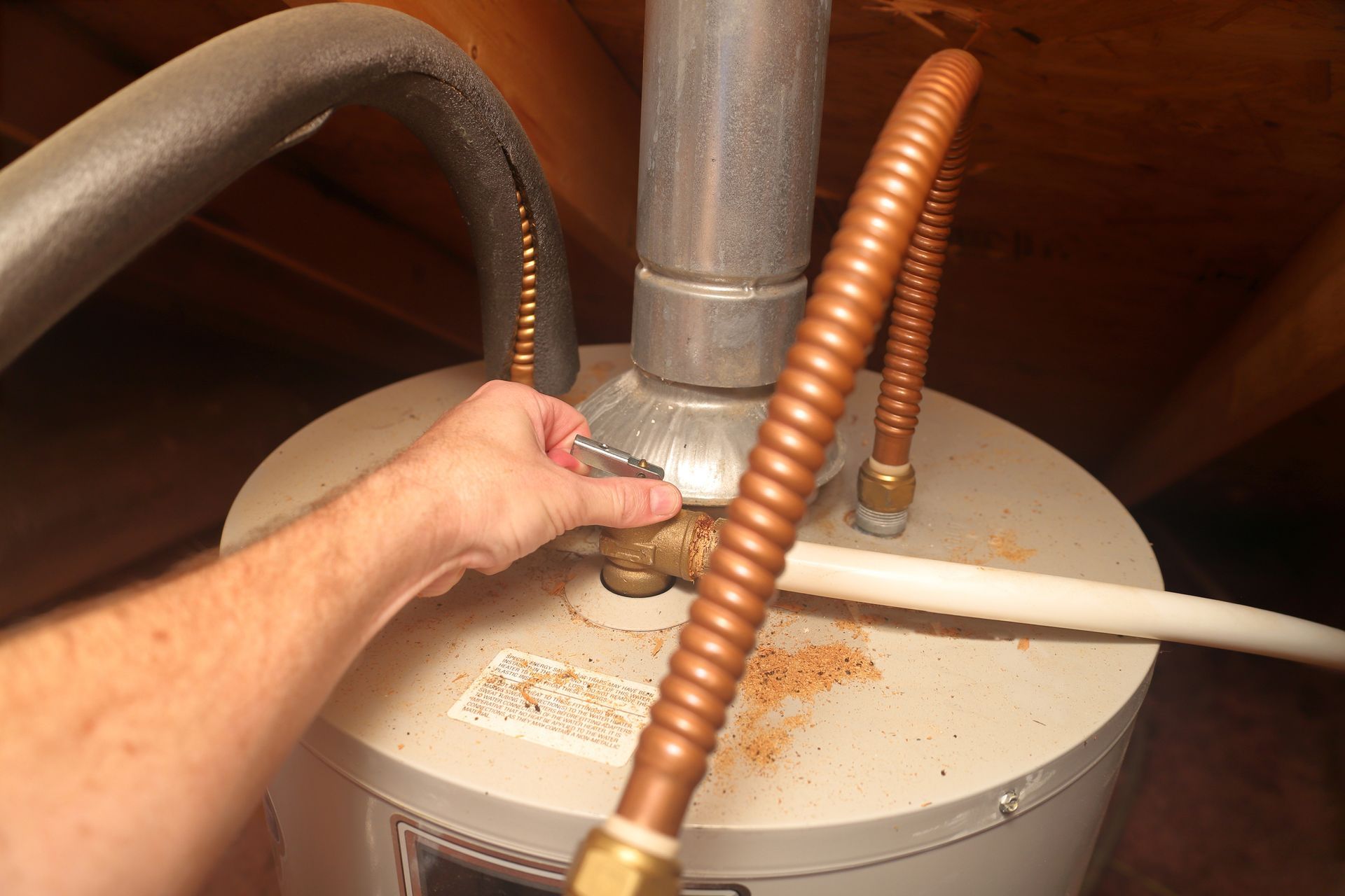 Hand adjusting a water heater connection with copper pipes on top of the tank