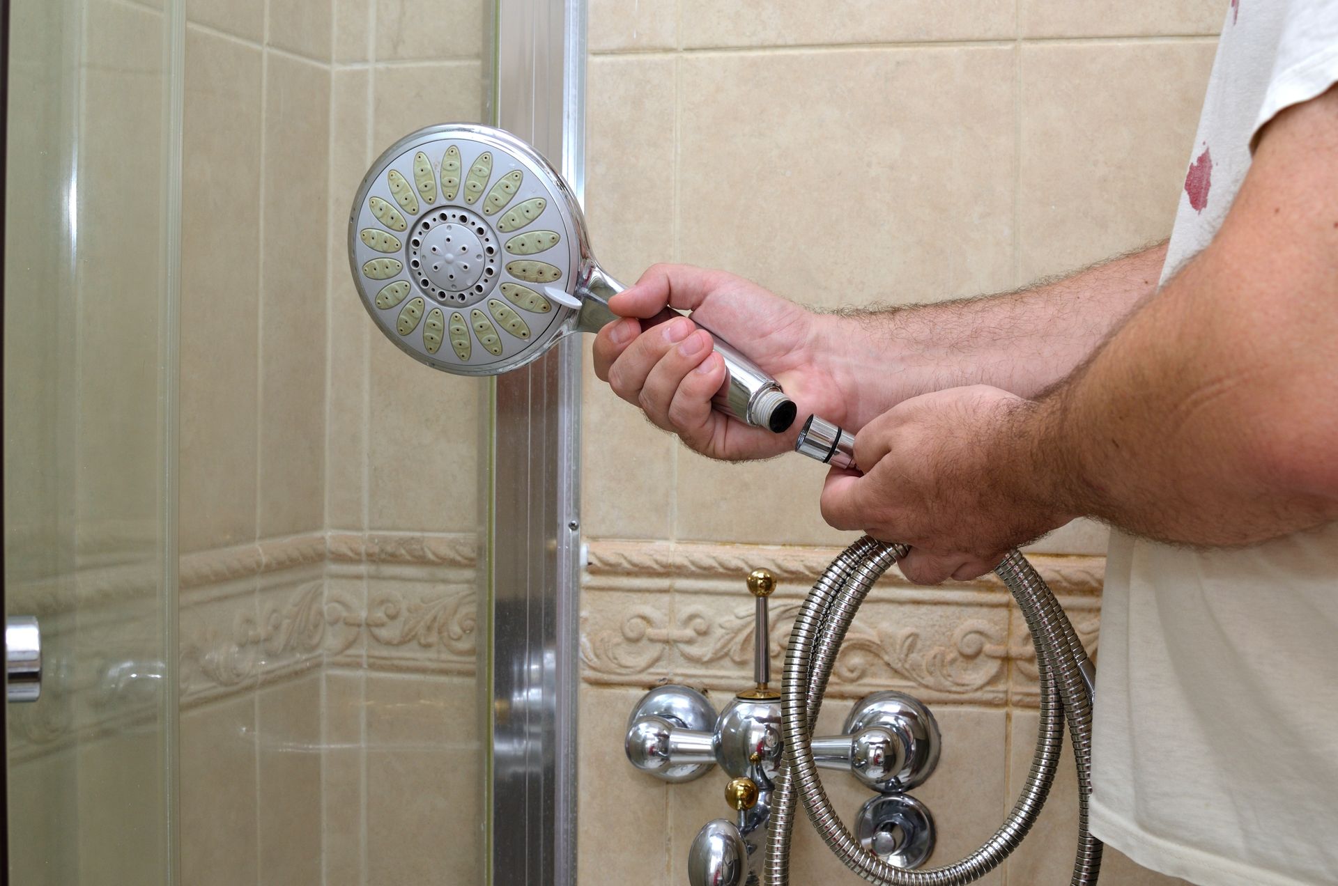 Person rinsing a showerhead in a tiled bathroom shower.