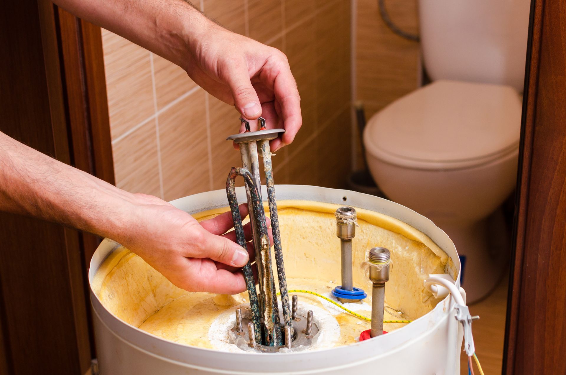 Hands installing a metal assembly into a yellow bucket in a small bathroom.