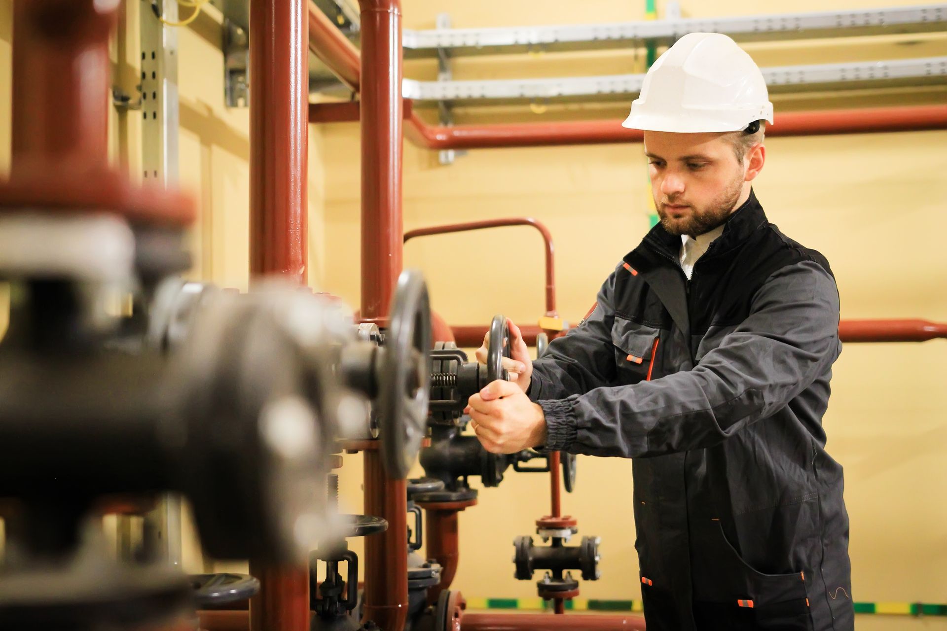 Worker in a hard hat adjusting industrial piping in a plant with red valves.
