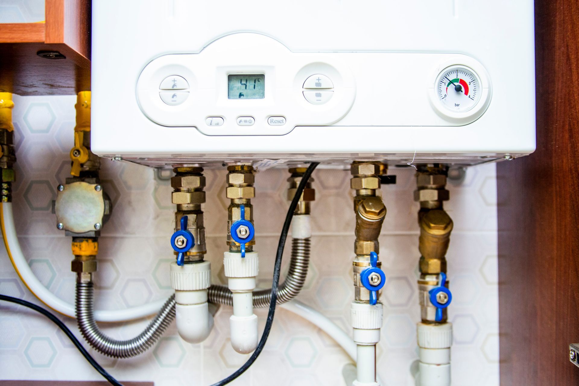 Wall-mounted boiler with digital display and pressure gauge, pipes and blue valves beneath it