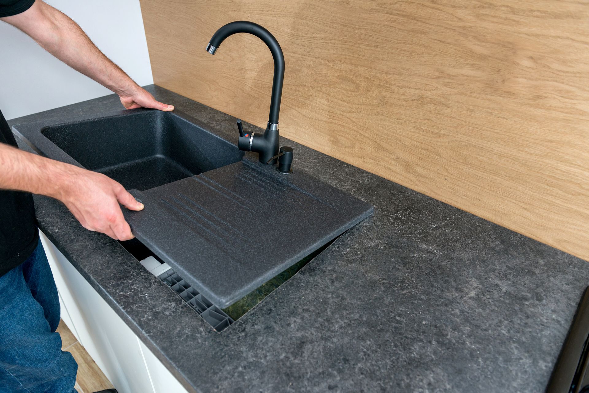 Hands positioning a black sink drying rack beside a black kitchen sink and faucet on a dark countertop