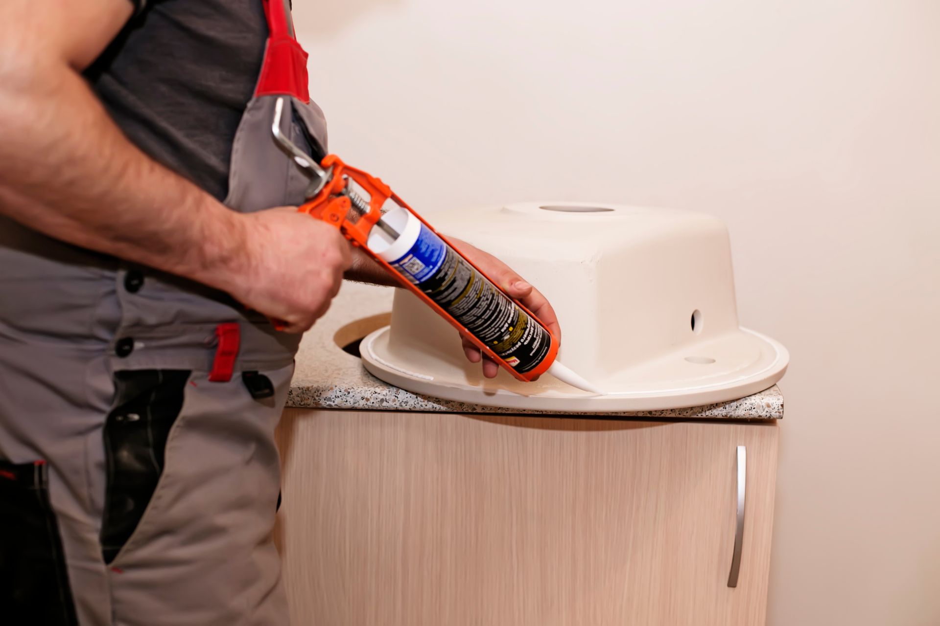 Person applying sealant around a sink on a bathroom countertop