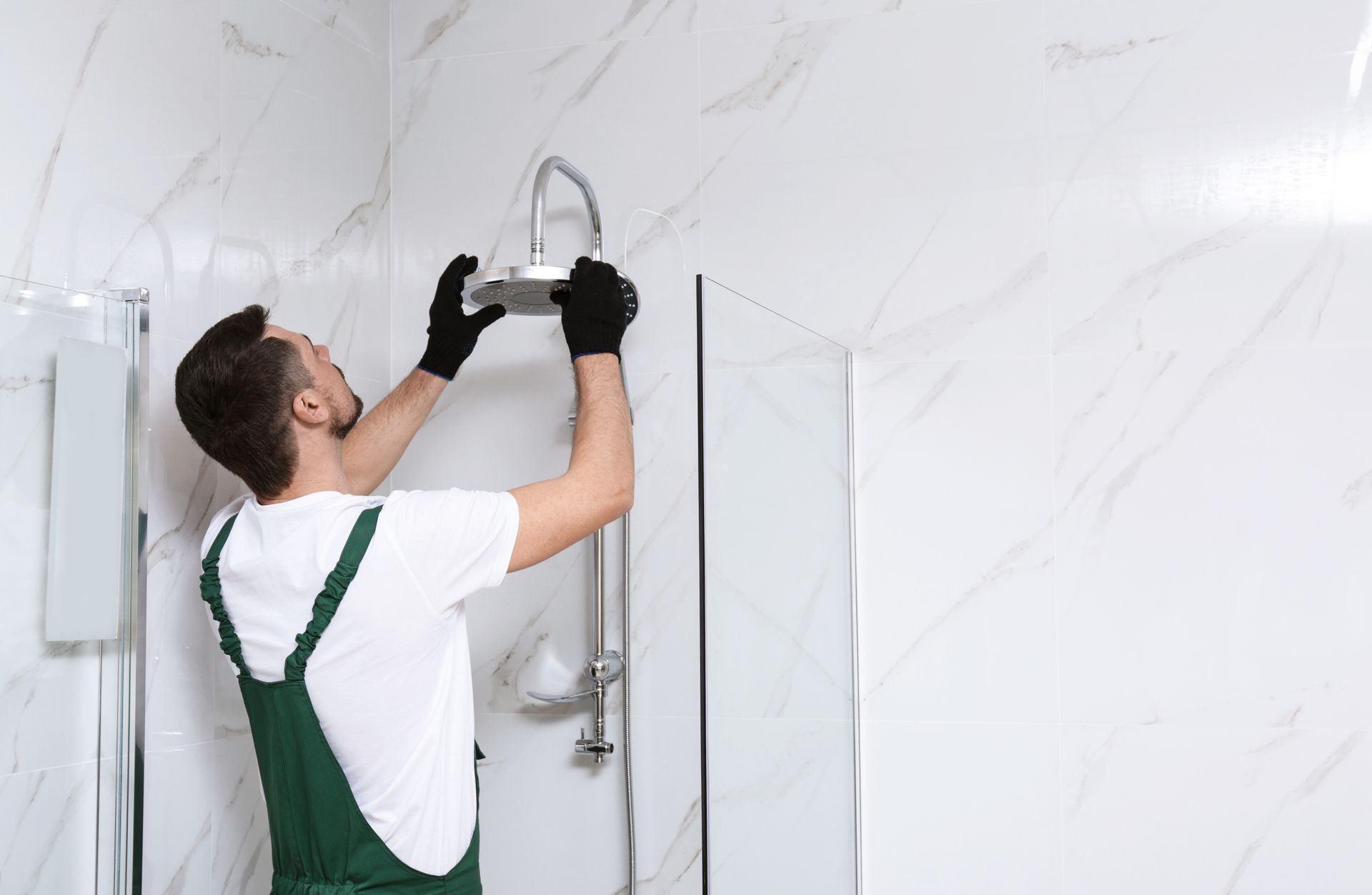 Technician in green overalls installing a shower fixture in a white tiled bathroom