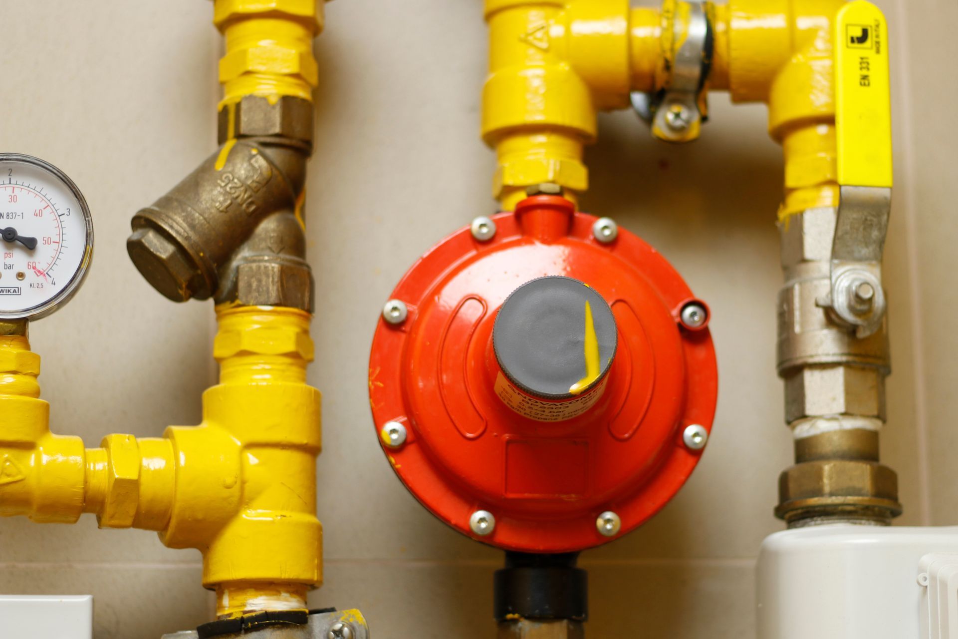 Yellow gas pipes with a red circular valve and pressure gauge on a wall