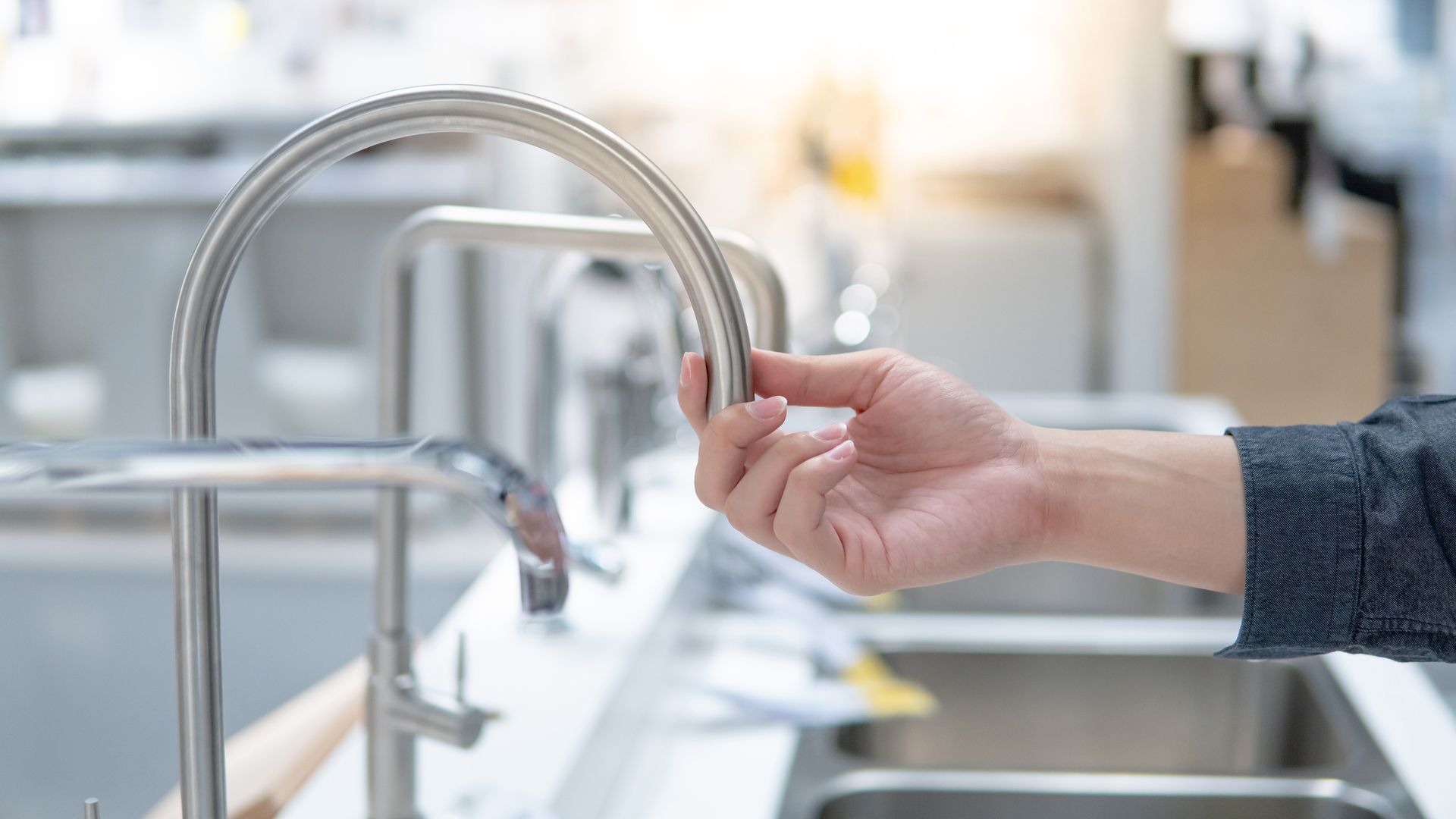 Hand turning on a curved chrome faucet over a kitchen sink