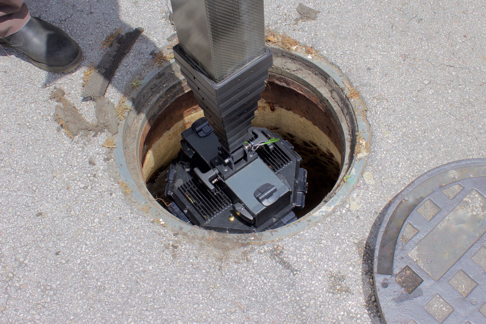 Camera being lowered into an open manhole on a concrete street.