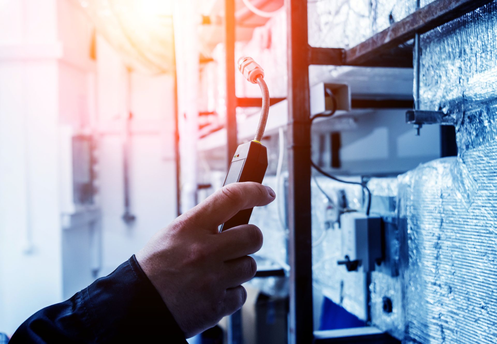 Hand holding a probe near electrical equipment in a blue-lit industrial setting