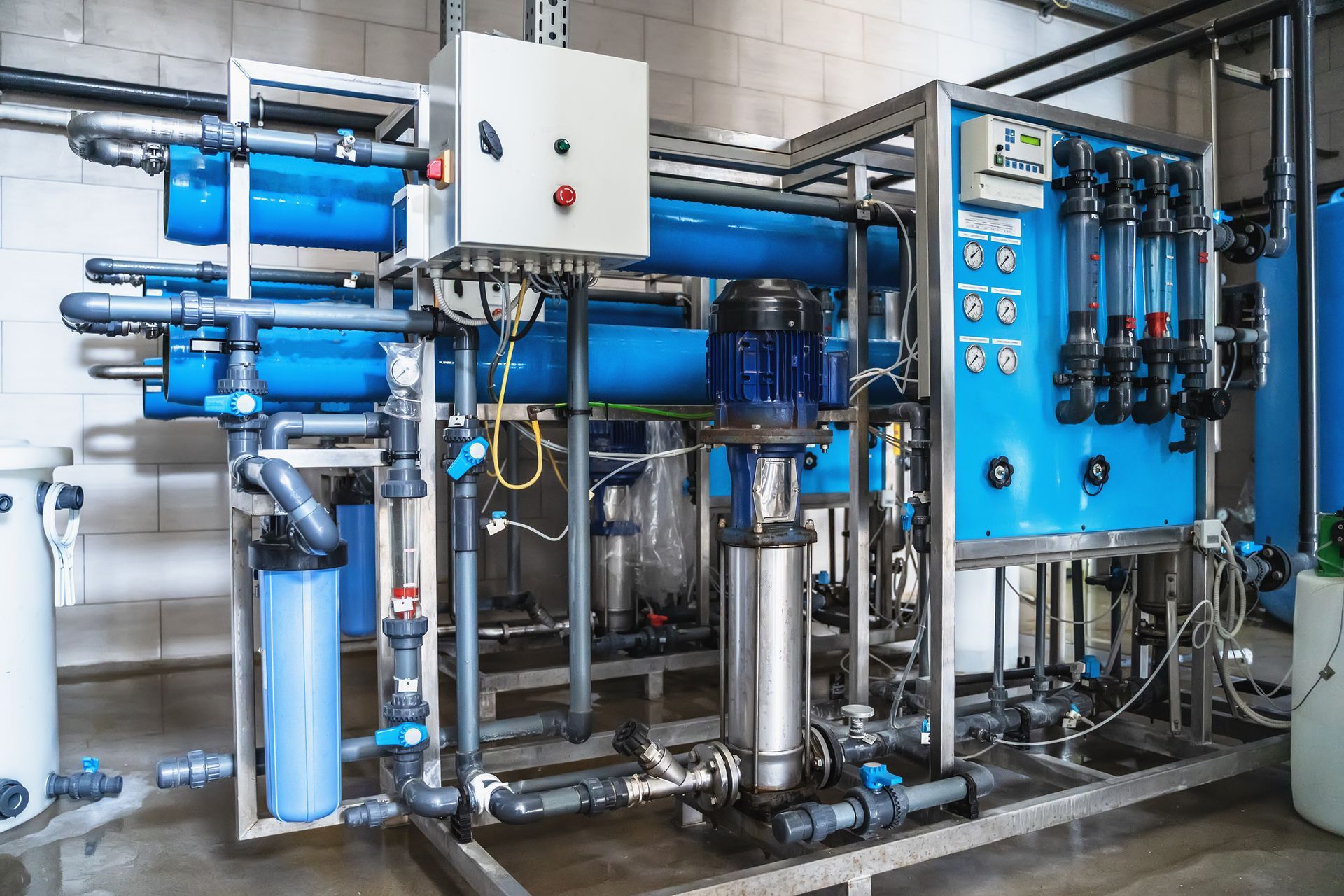 Industrial water filtration system with blue pipes, tanks, and control panel in a utility room