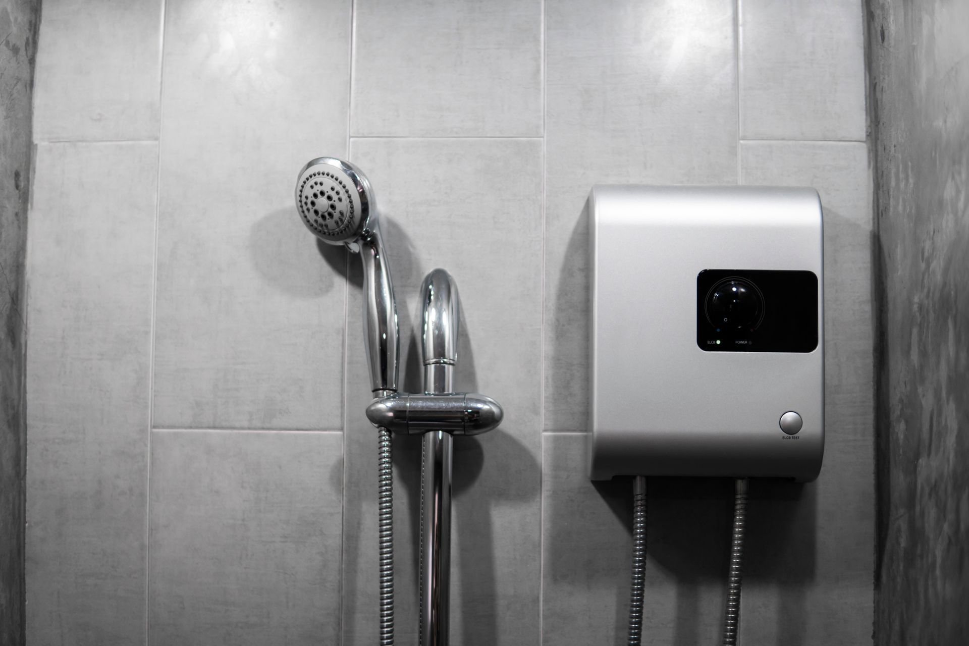 Shower wall with handheld showerhead and chrome faucet beside a white water heater unit