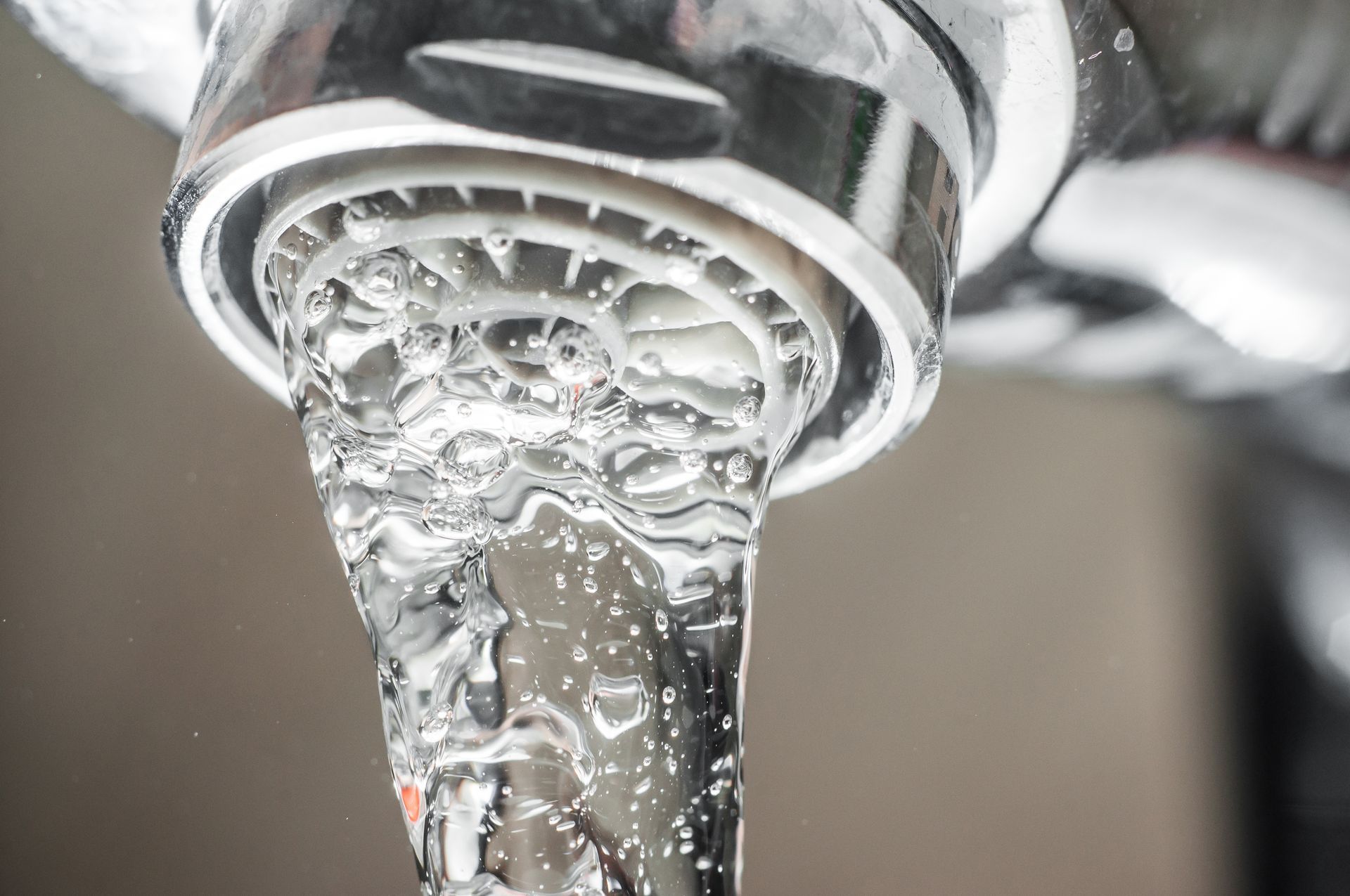 Close-up of water flowing from a chrome faucet, with droplets and bubbles visible