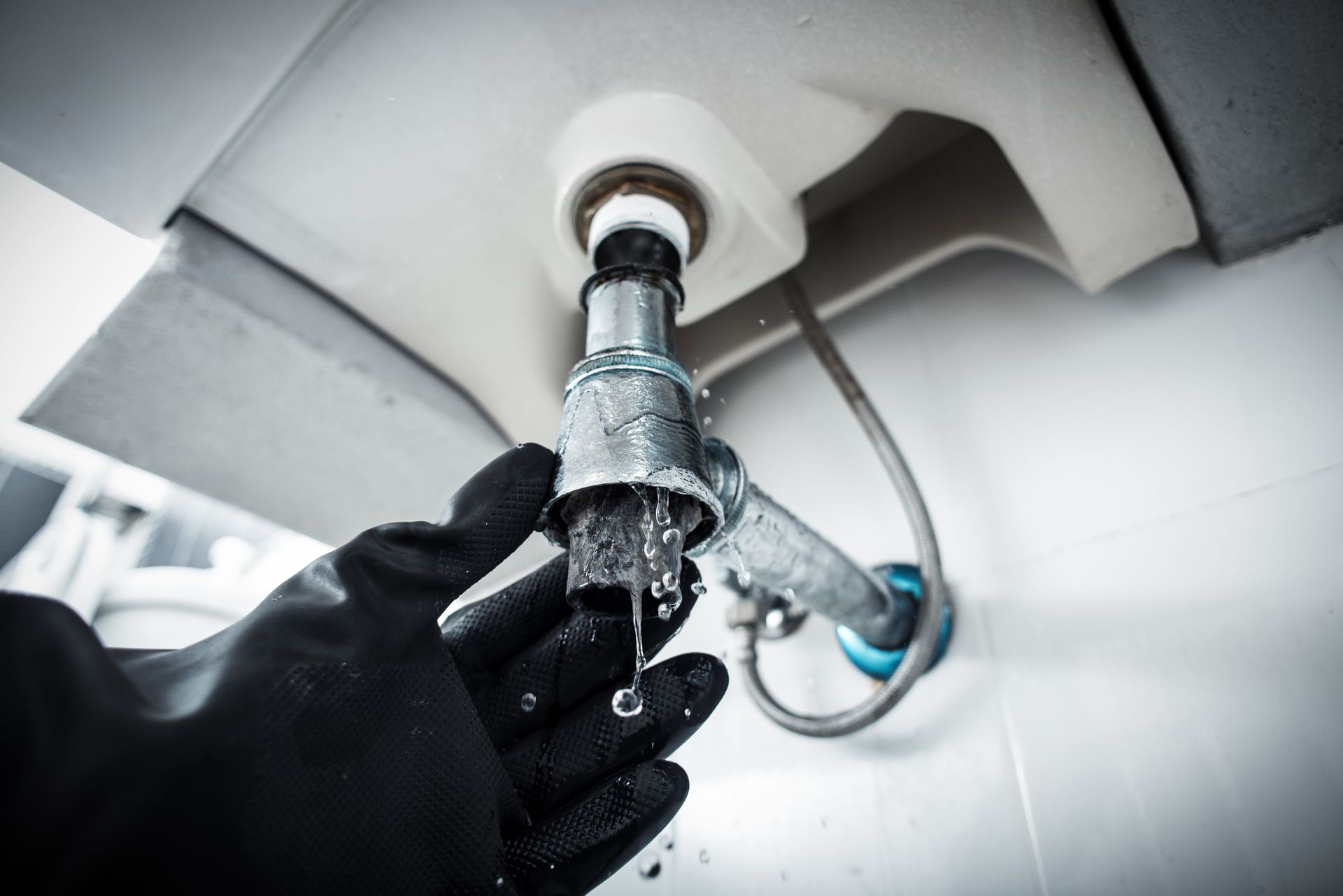 Gloved hands repairing a leaky sink drain under a white bathroom sink