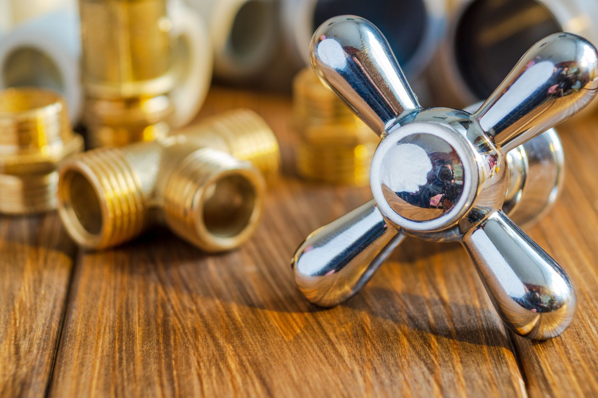 Chrome faucet handles and brass plumbing fittings on a wooden surface