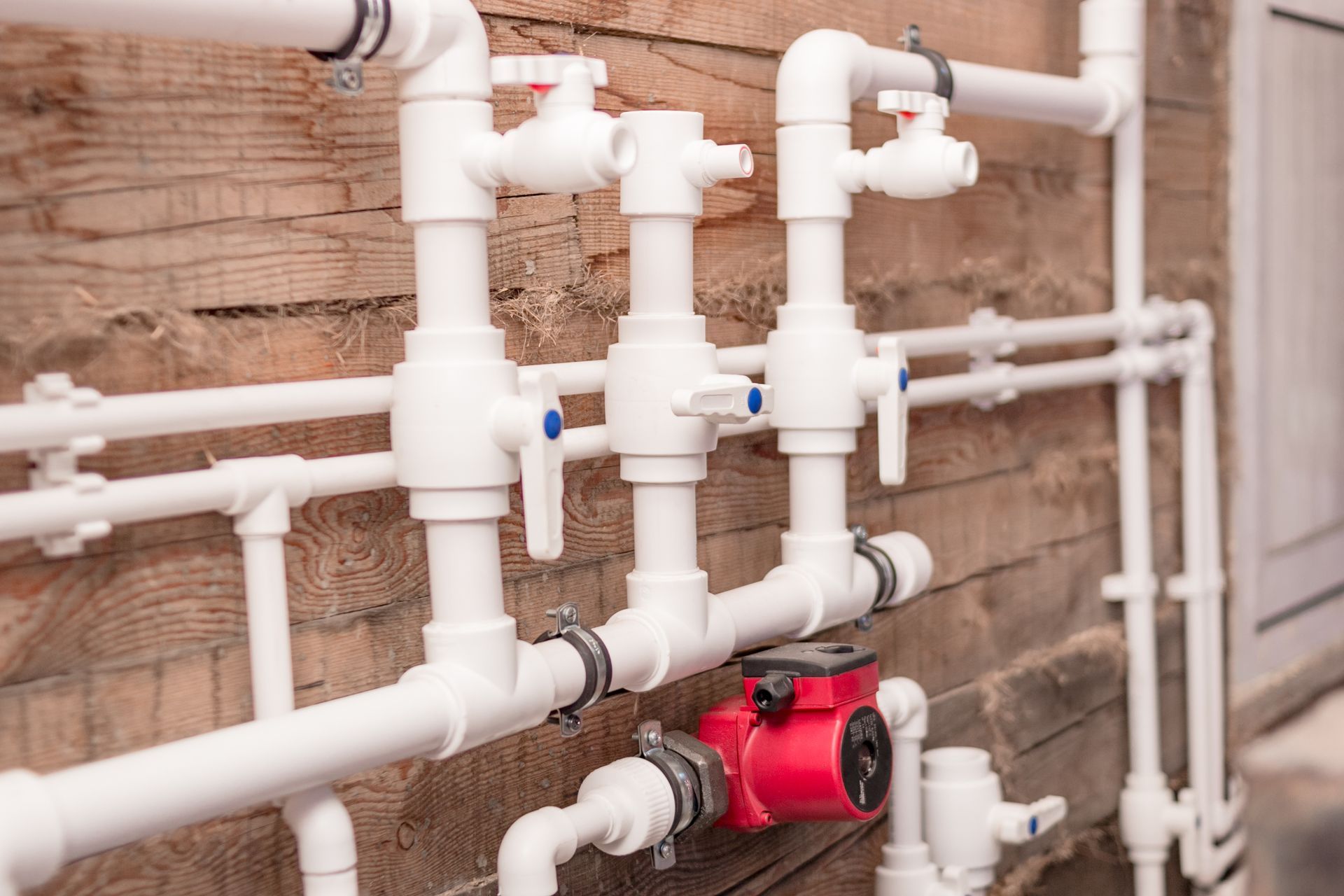White plumbing pipes and valves on a brick wall with a red pump in the foreground