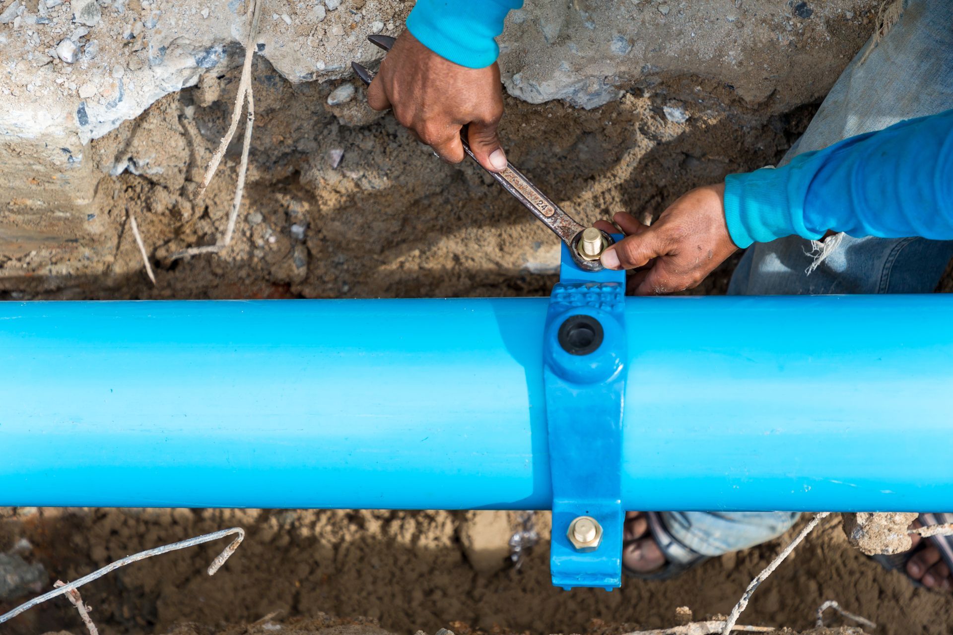 Workers tightening a clamp on a blue underground pipe in a trench