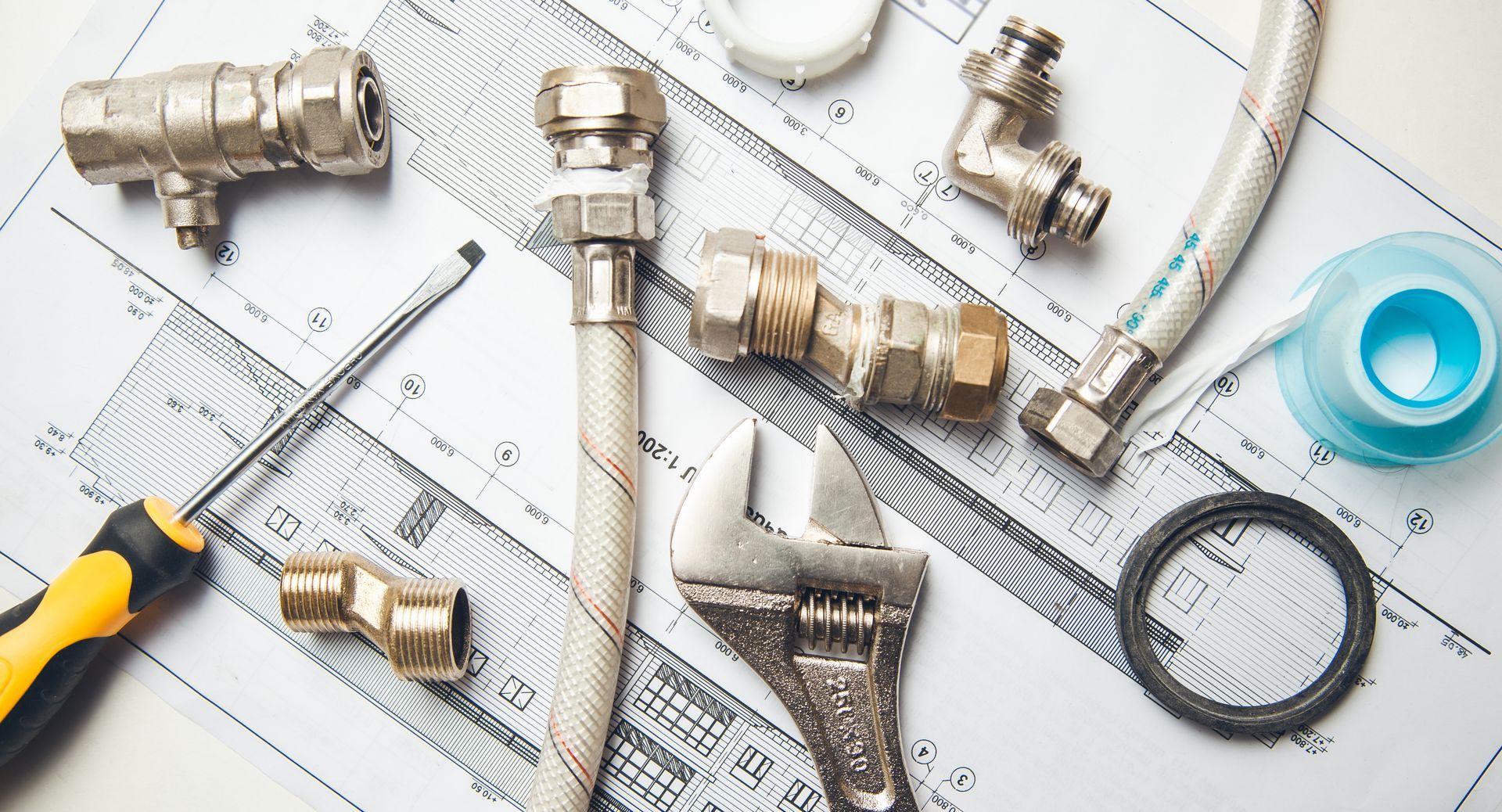 Plumbing tools and brass fittings arranged on a white work surface with a tape measure and wrench