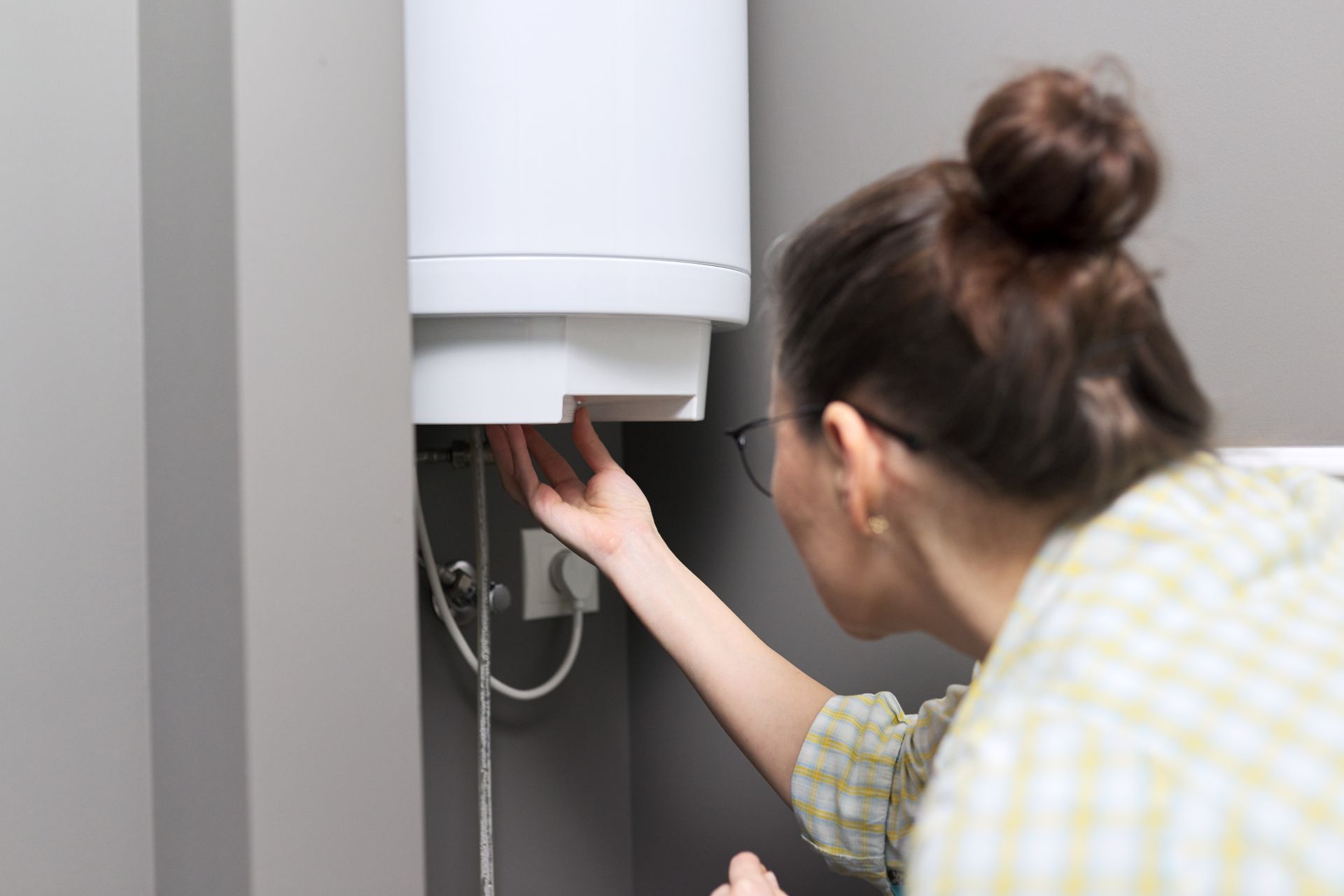 Person inspecting wiring under a wall-mounted boiler in a home utility room