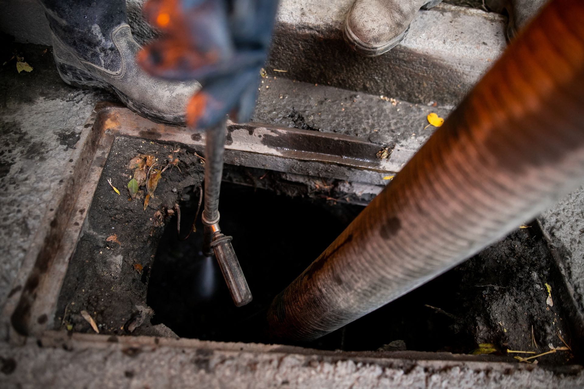 Rusty metal pipes over an open manhole in concrete ground