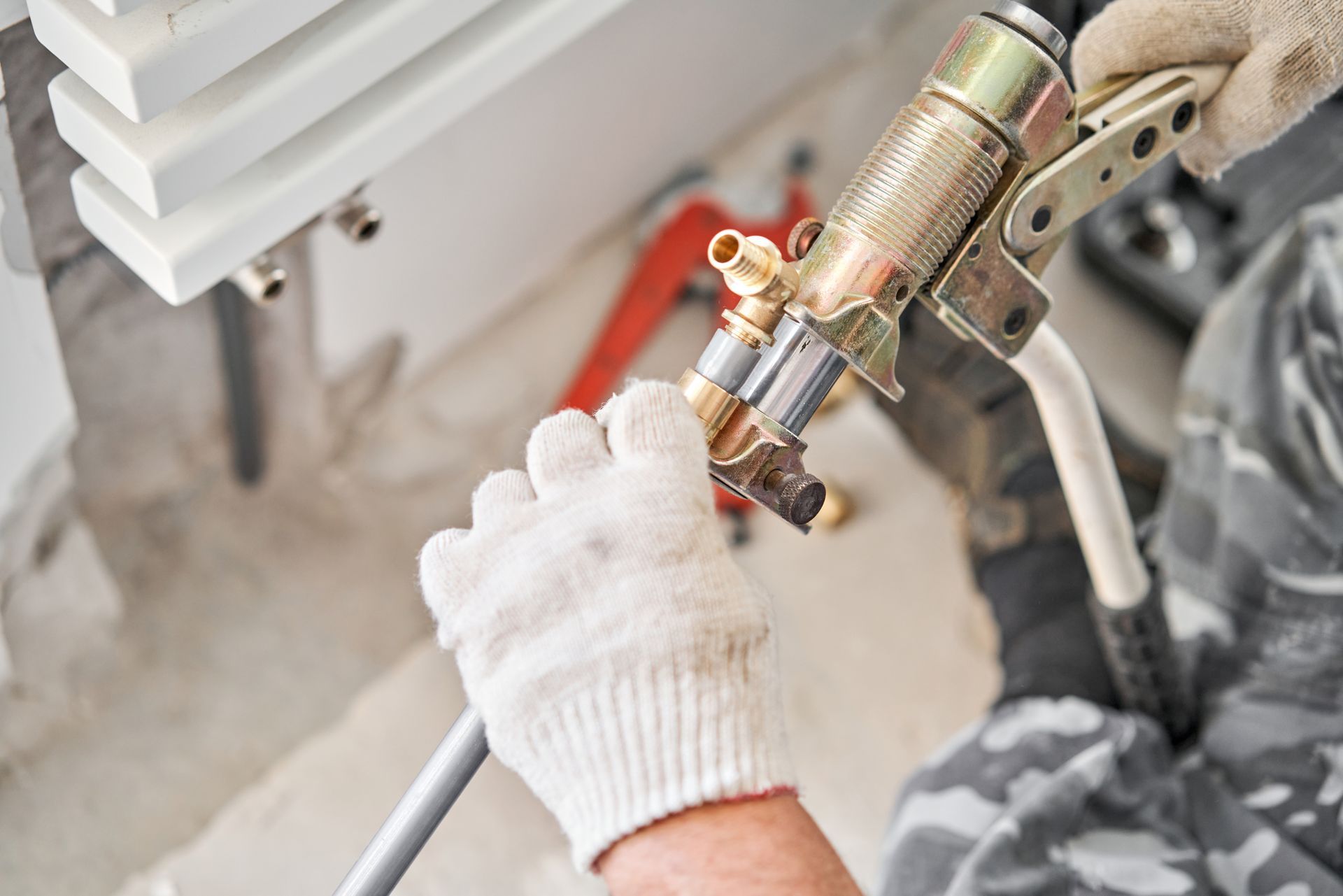 Gloved hand spray-painting a metal pipe with a paint gun near a white vent cover