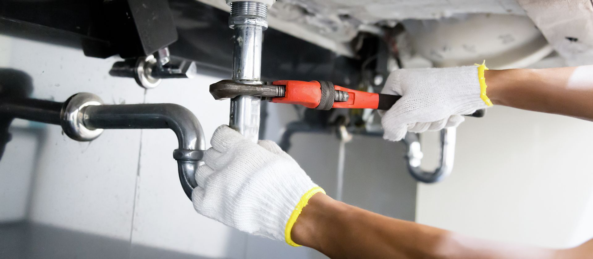 Gloved hands tightening a pipe fitting under a vehicle with a red tool