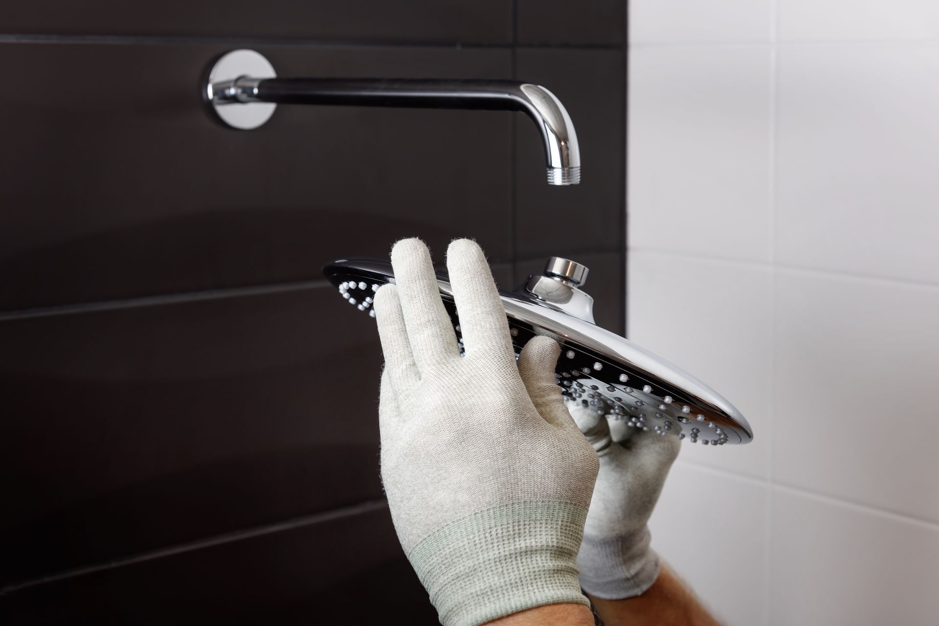 Gloved hands polishing a chrome shower head in a tiled bathroom