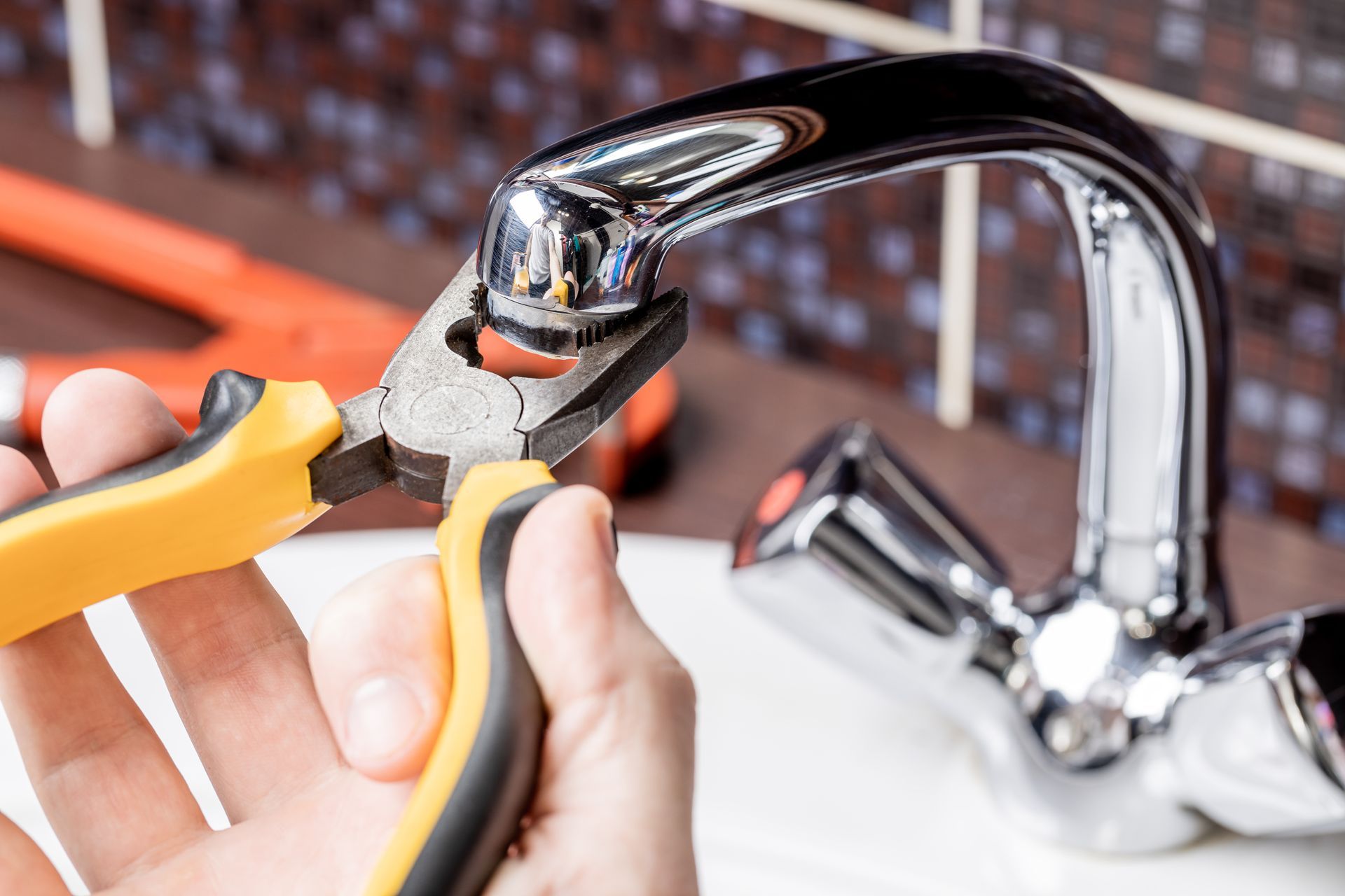 Hands using pliers to repair a chrome faucet sink fixture