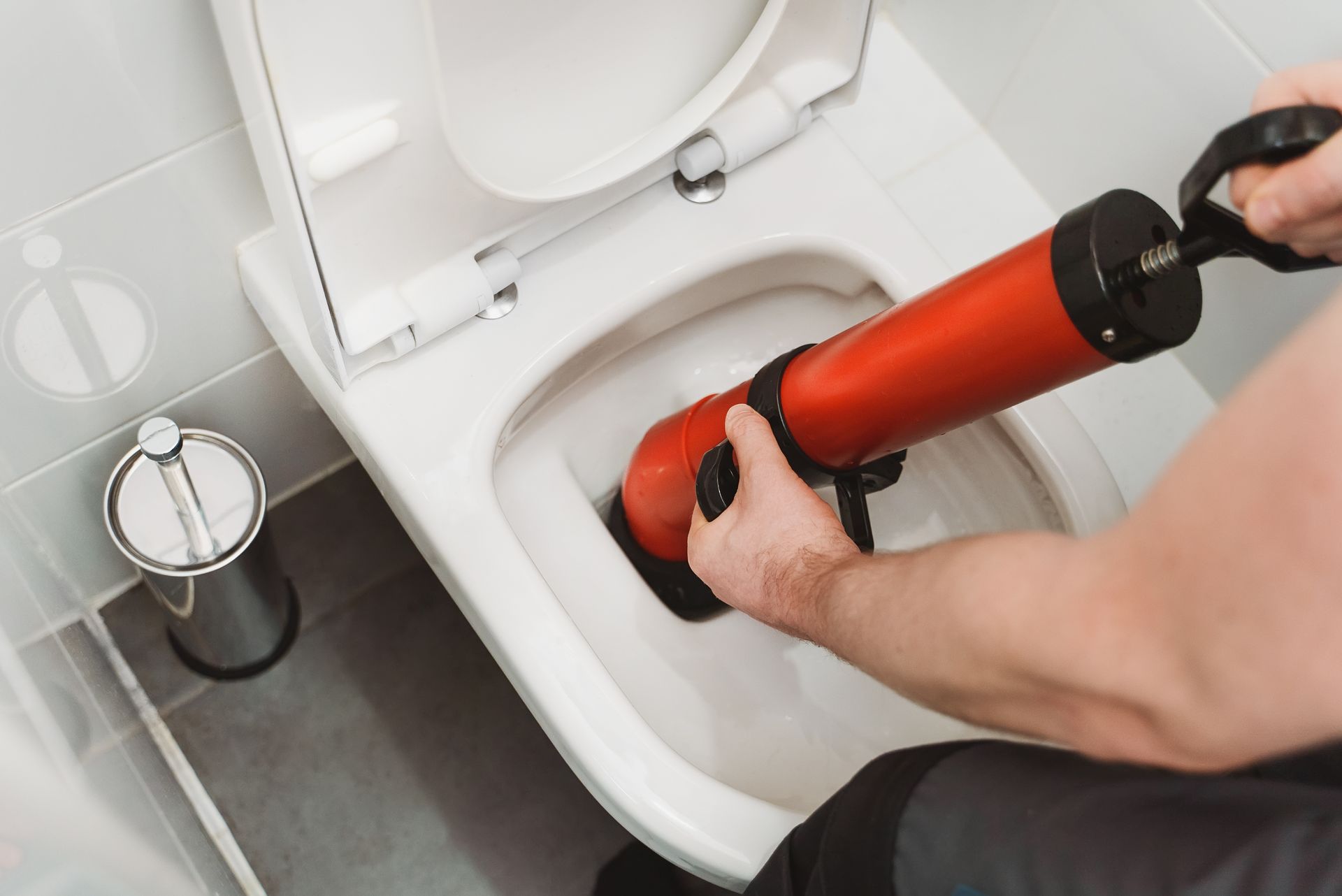 Person using a red plunger to unclog a toilet in a bathroom