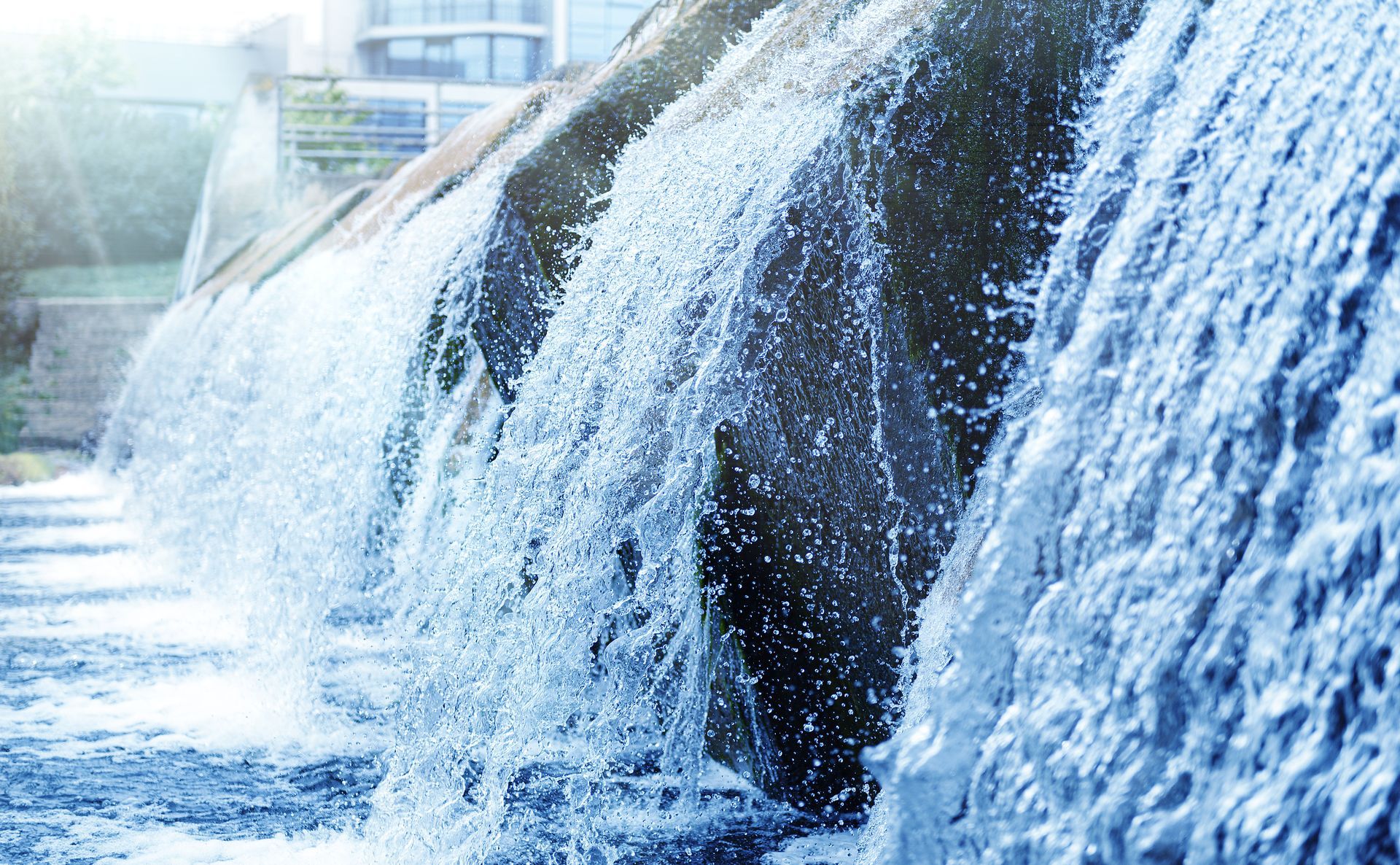 Cascading waterfall over dark rocks in a bright blue urban water feature