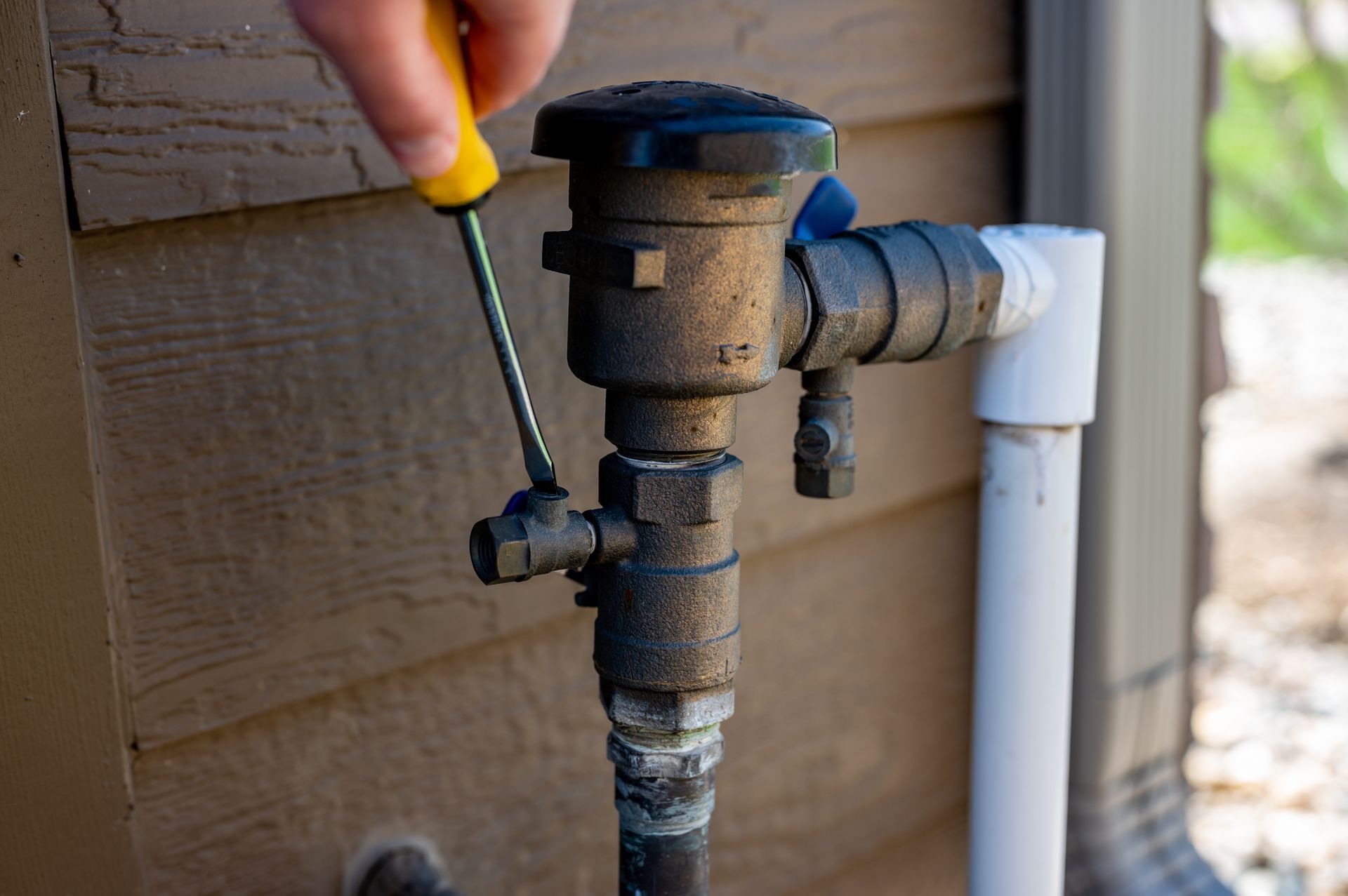 Hand turning a valve on a water pipe beside a house exterior