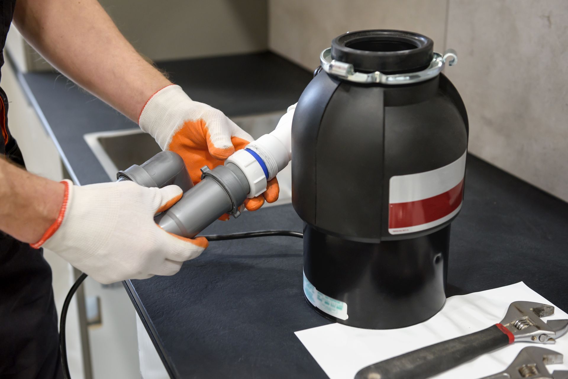 Gloved hands working on a black cylindrical machine with tools on a workbench