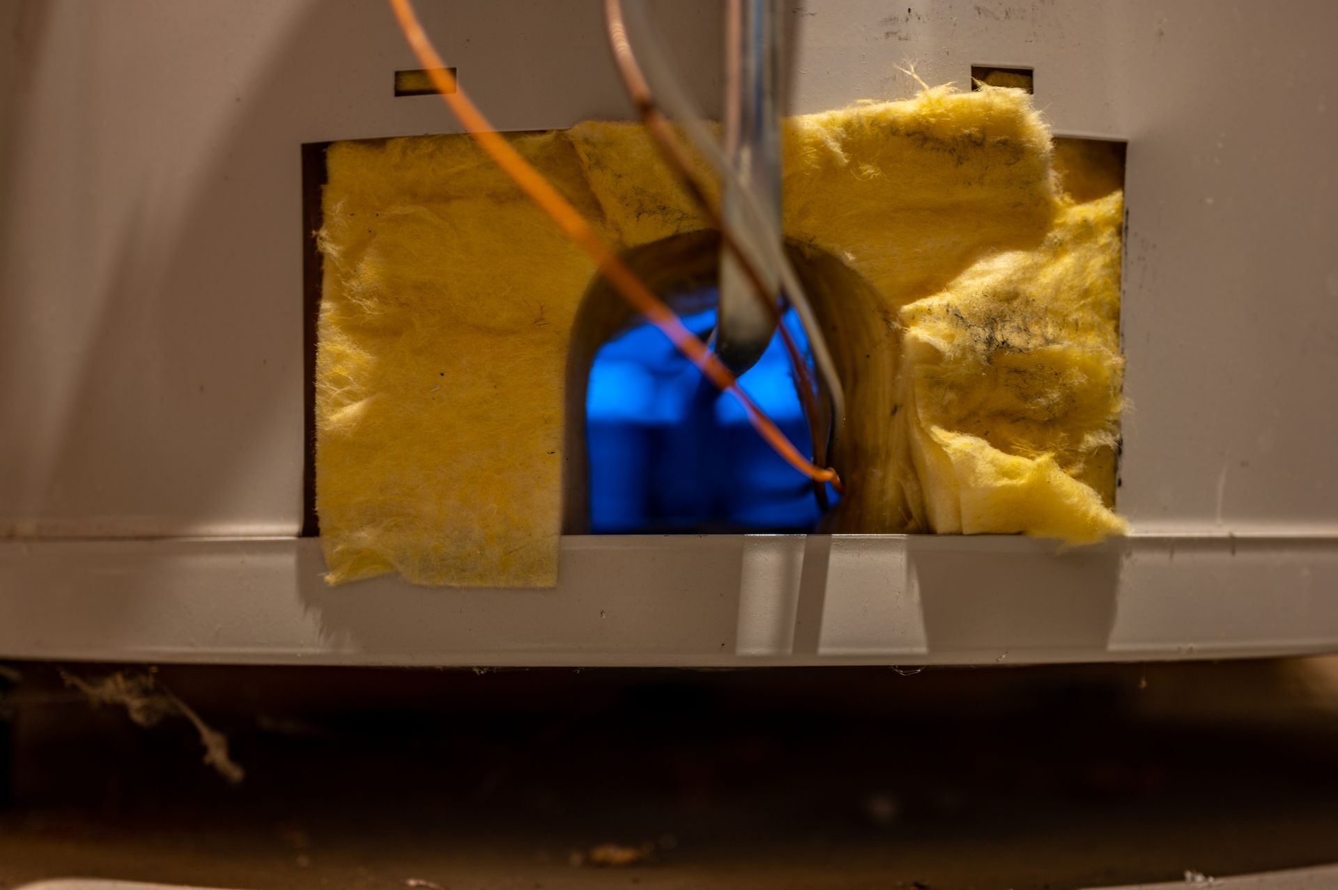 Yellow insulation around a small opening with a blue flame behind it and a wire crossing the center