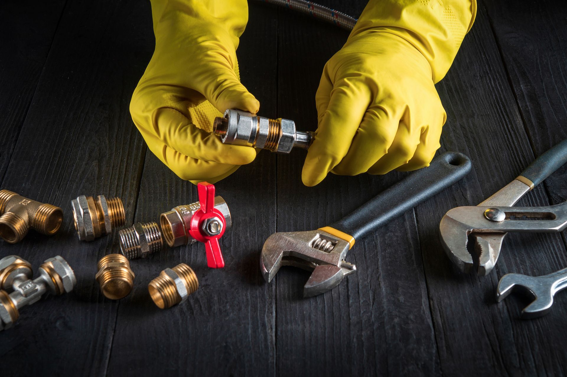 Yellow-gloved hands assembling plumbing fittings on a dark workbench with tools nearby