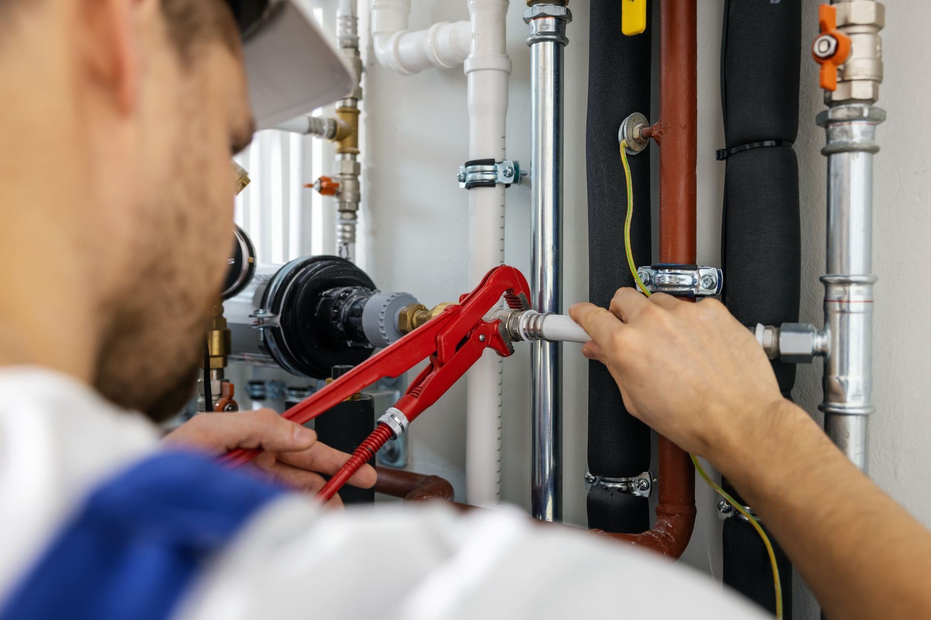 Technician using red pipe wrench to repair plumbing pipes and valves in a utility room