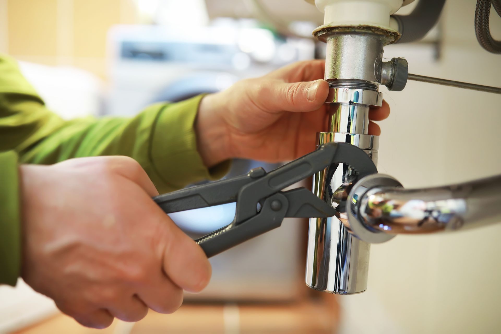 Hands using pliers to tighten a chrome pipe fitting under a sink
