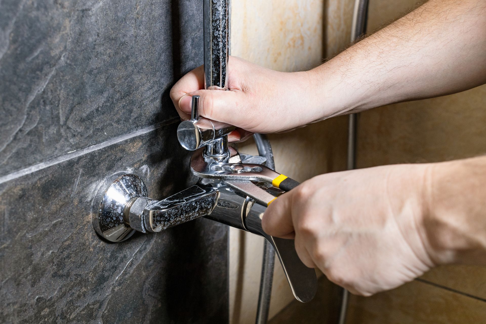 Hands using a wrench to tighten a chrome shower fixture against a tiled wall.