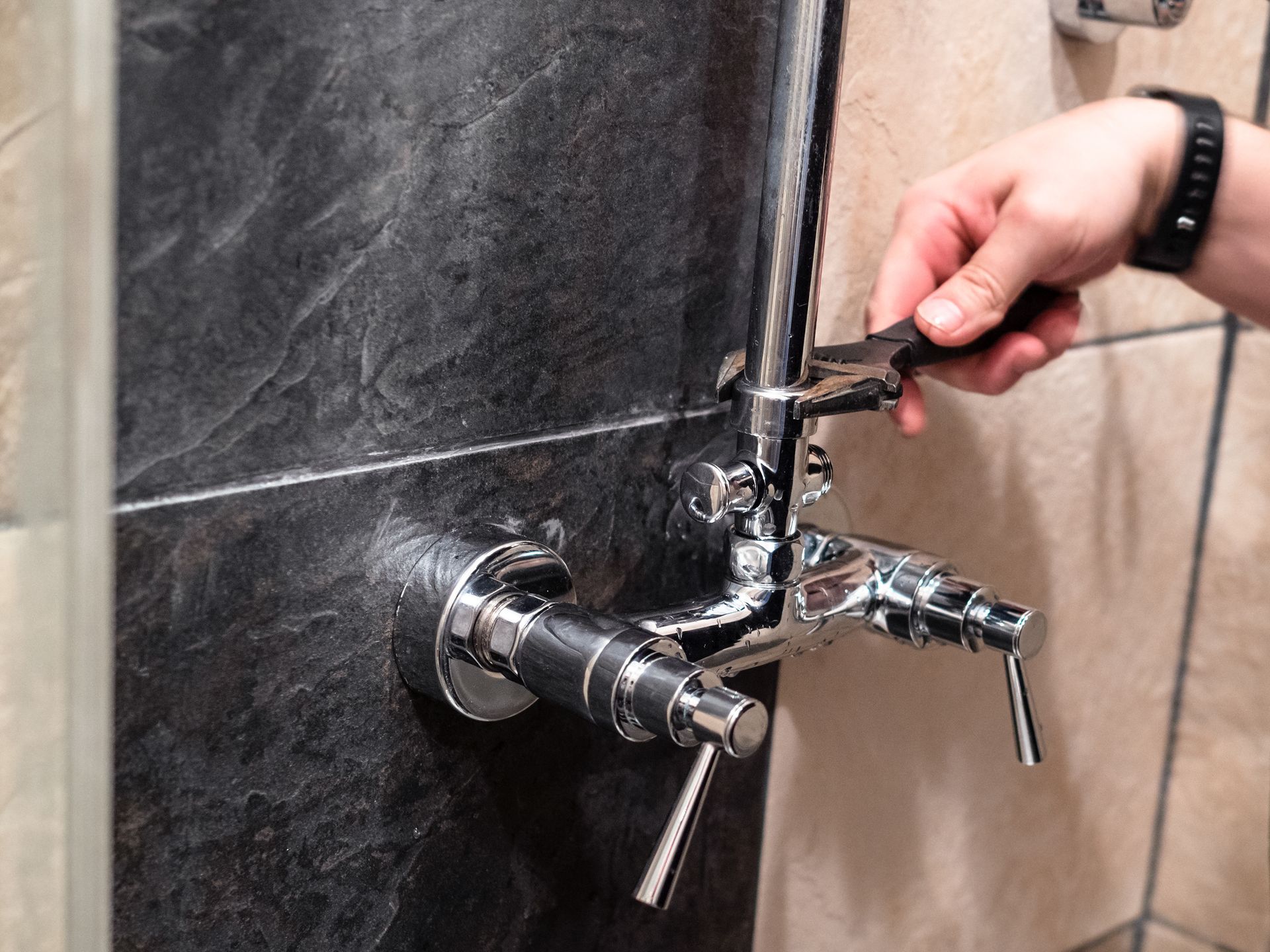 Person using a wrench to tighten a shower fixture with water spraying from the wall connection