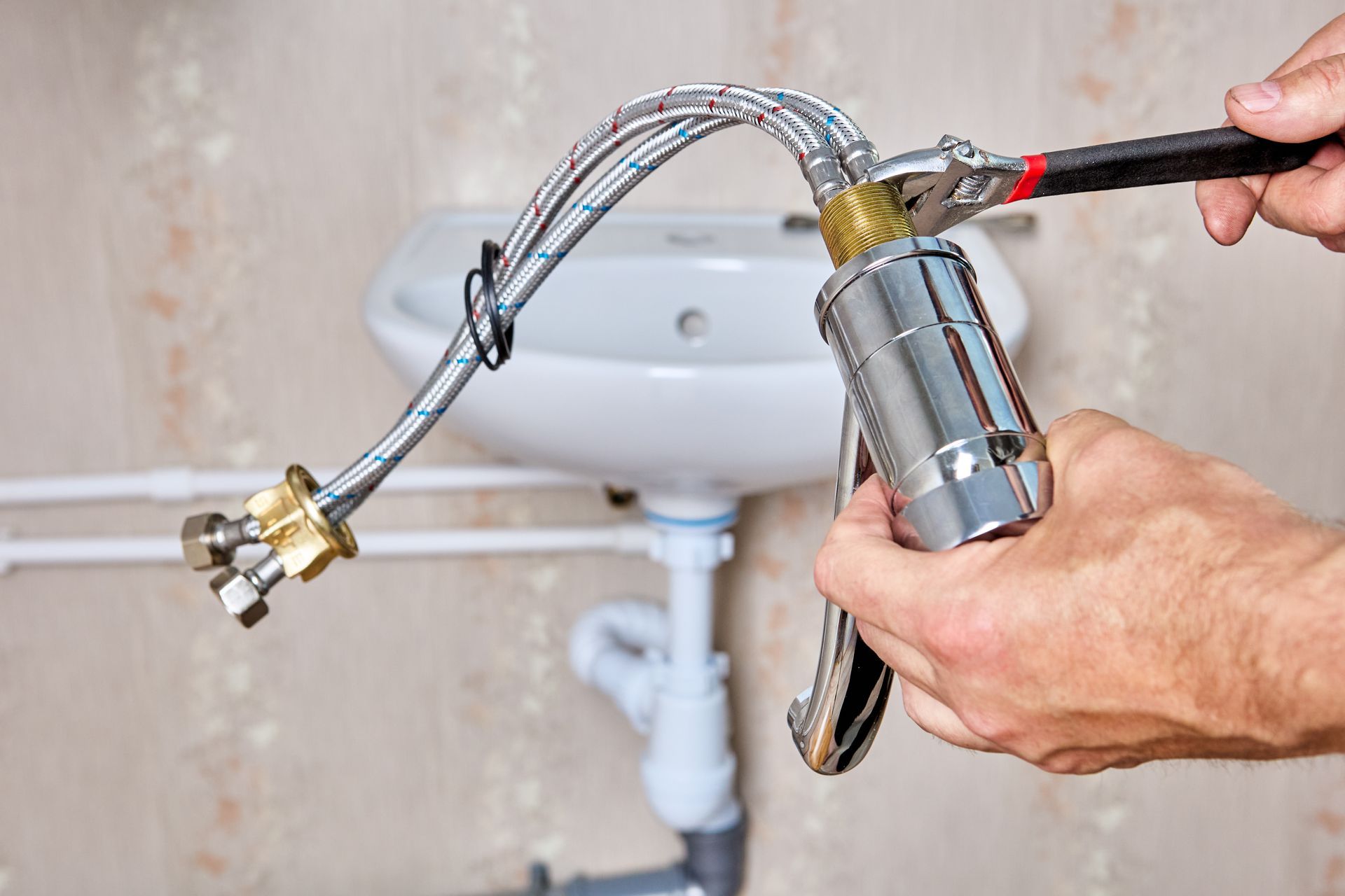 Hands using a tool to tighten a flexible faucet hose under a bathroom sink