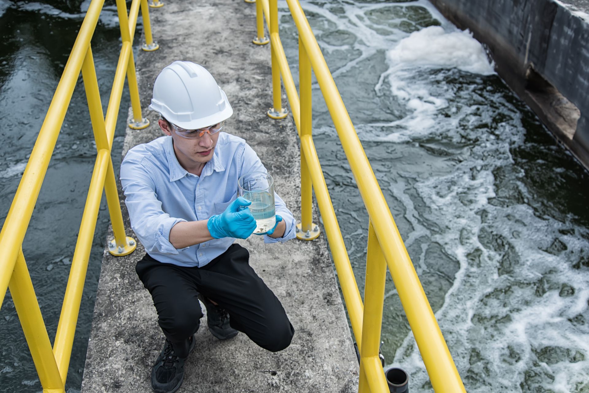 Worker in hard hat taking a water sample beside a foamy treatment channel