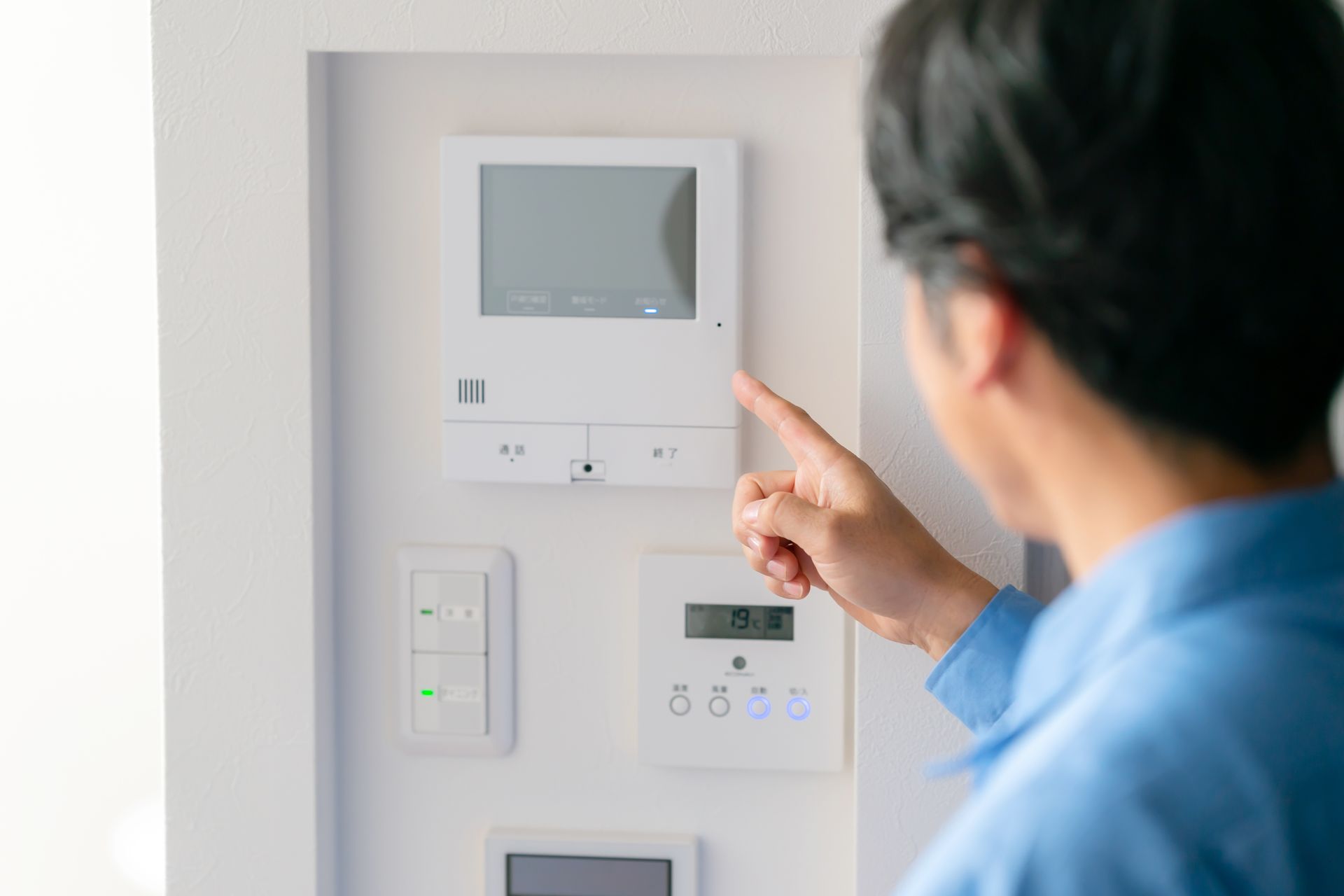 Person pointing at a wall-mounted home control panel in a bright hallway