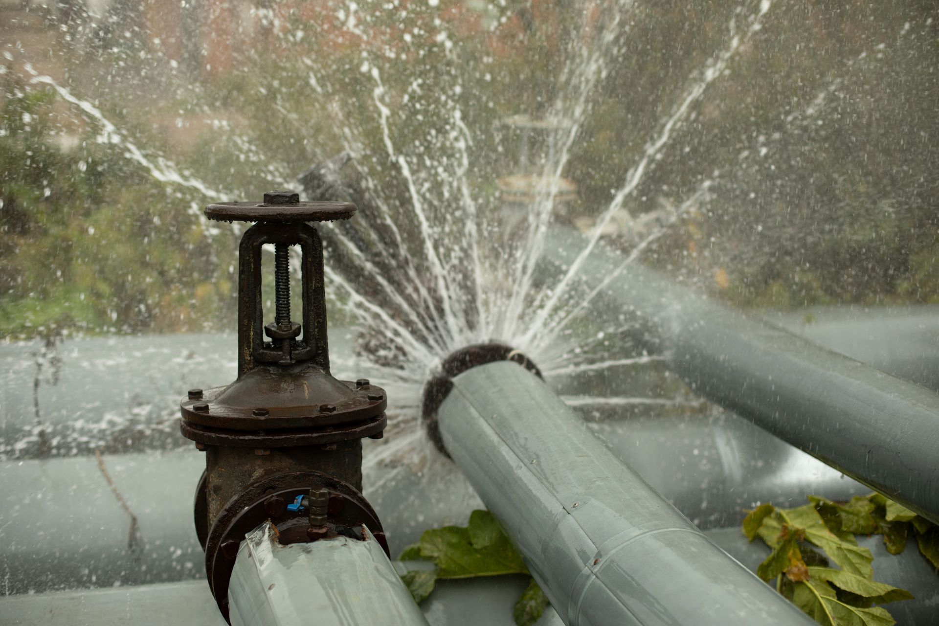 Water spraying from broken pipes beside a rusty valve in an outdoor industrial setting