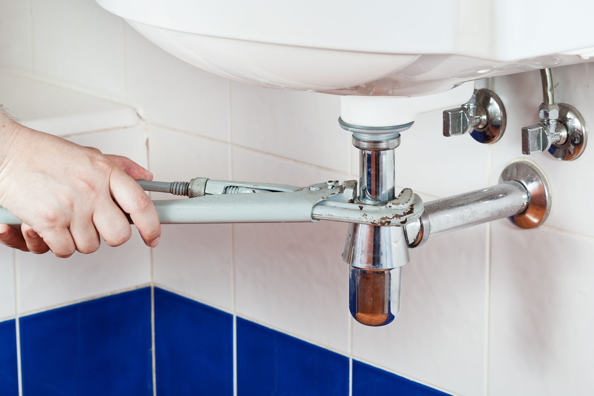 Person using a wrench to repair a bathroom sink drain pipe under a white sink.