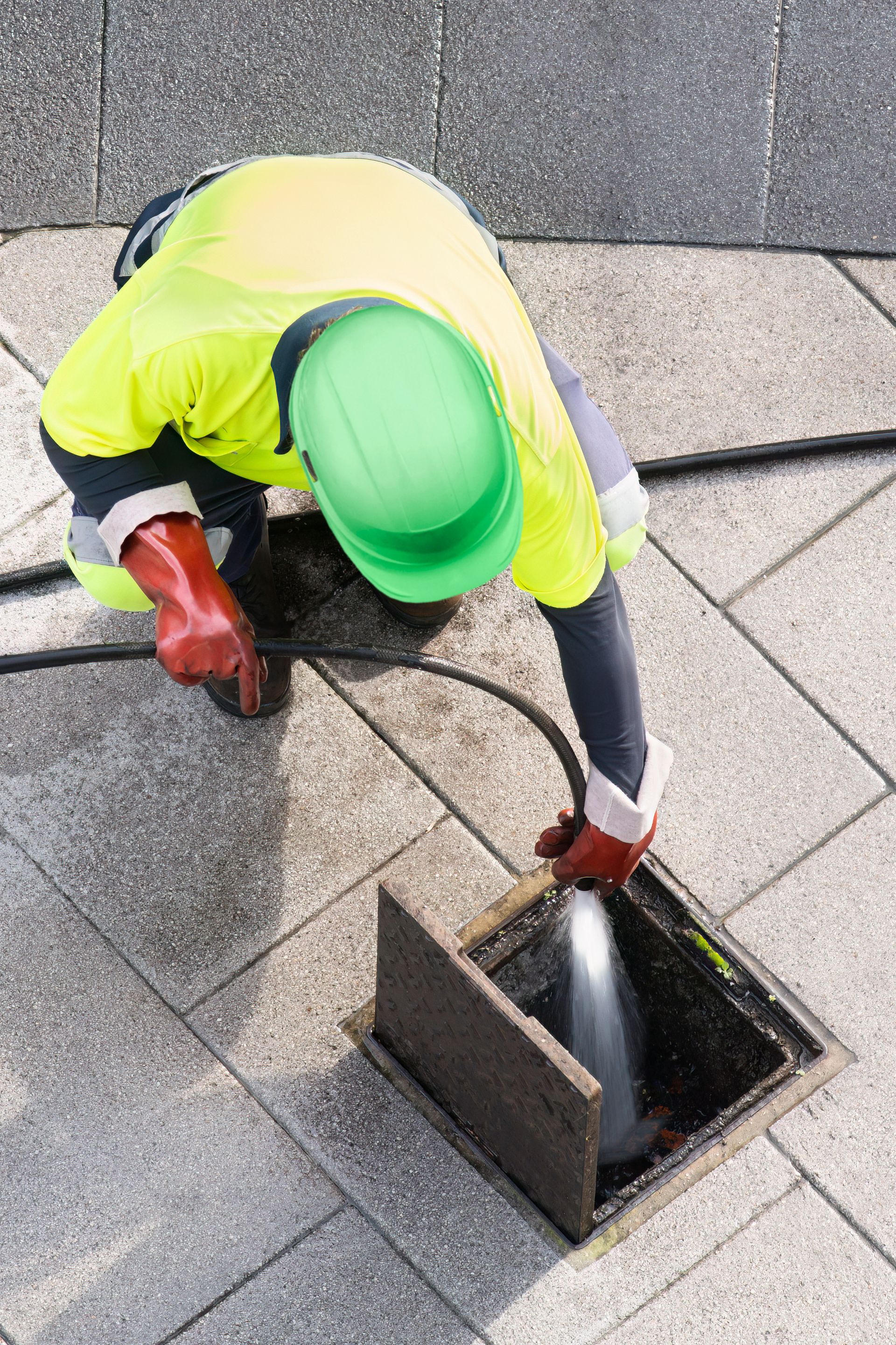 Worker in neon safety vest cleaning a rooftop drain with a hose.