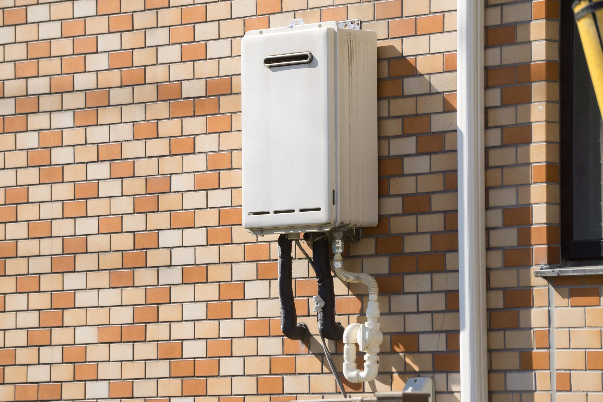 Wall-mounted white utility box and pipes on a brick building exterior