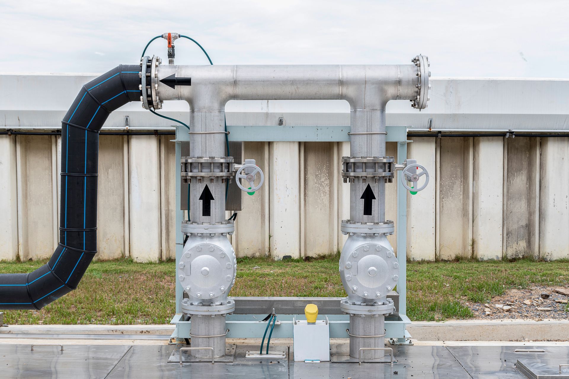 Industrial pipes and valves in a utility area, with a large black hose connected on the left.