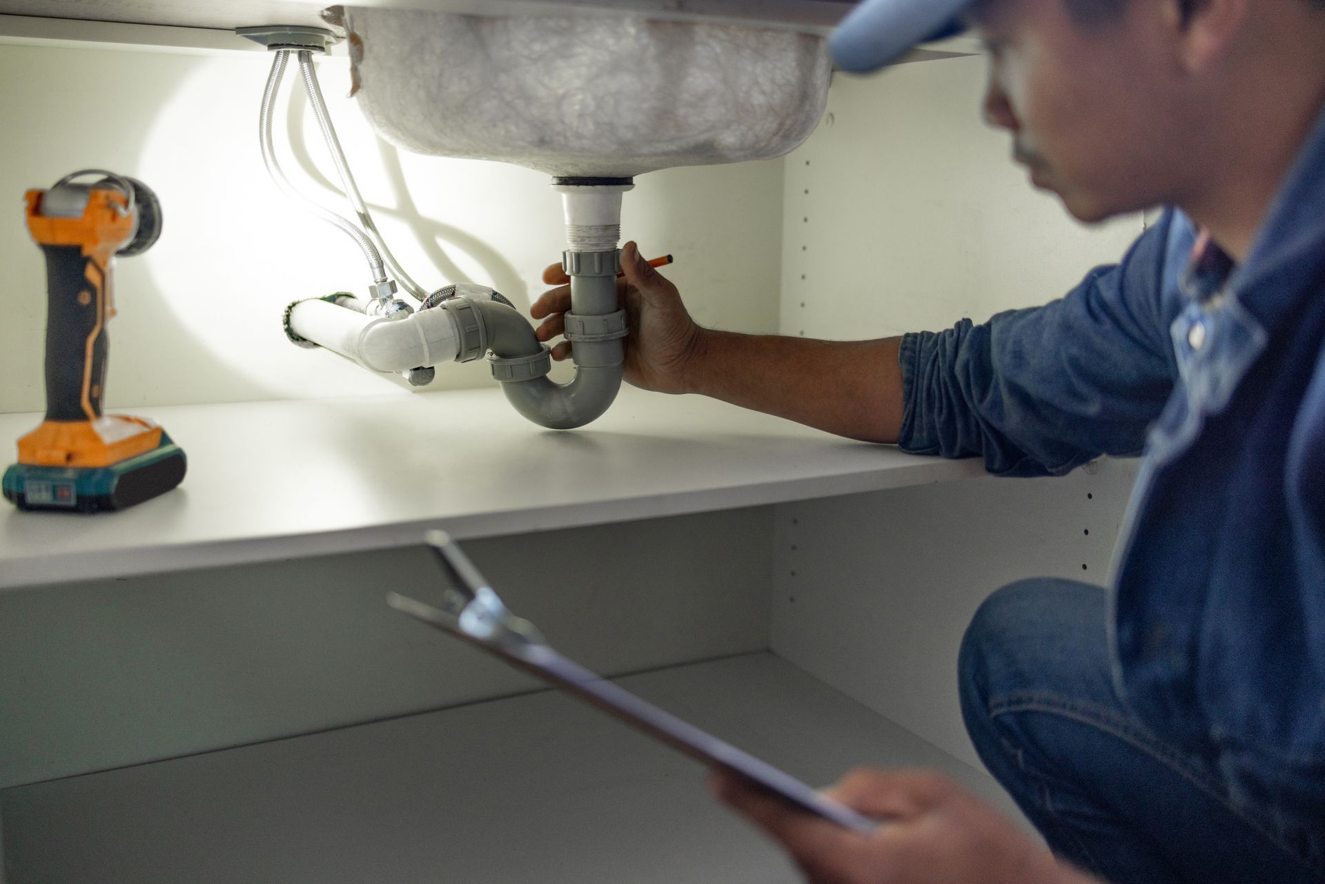 Technician repairing a sink drain under a cabinet, with tools nearby