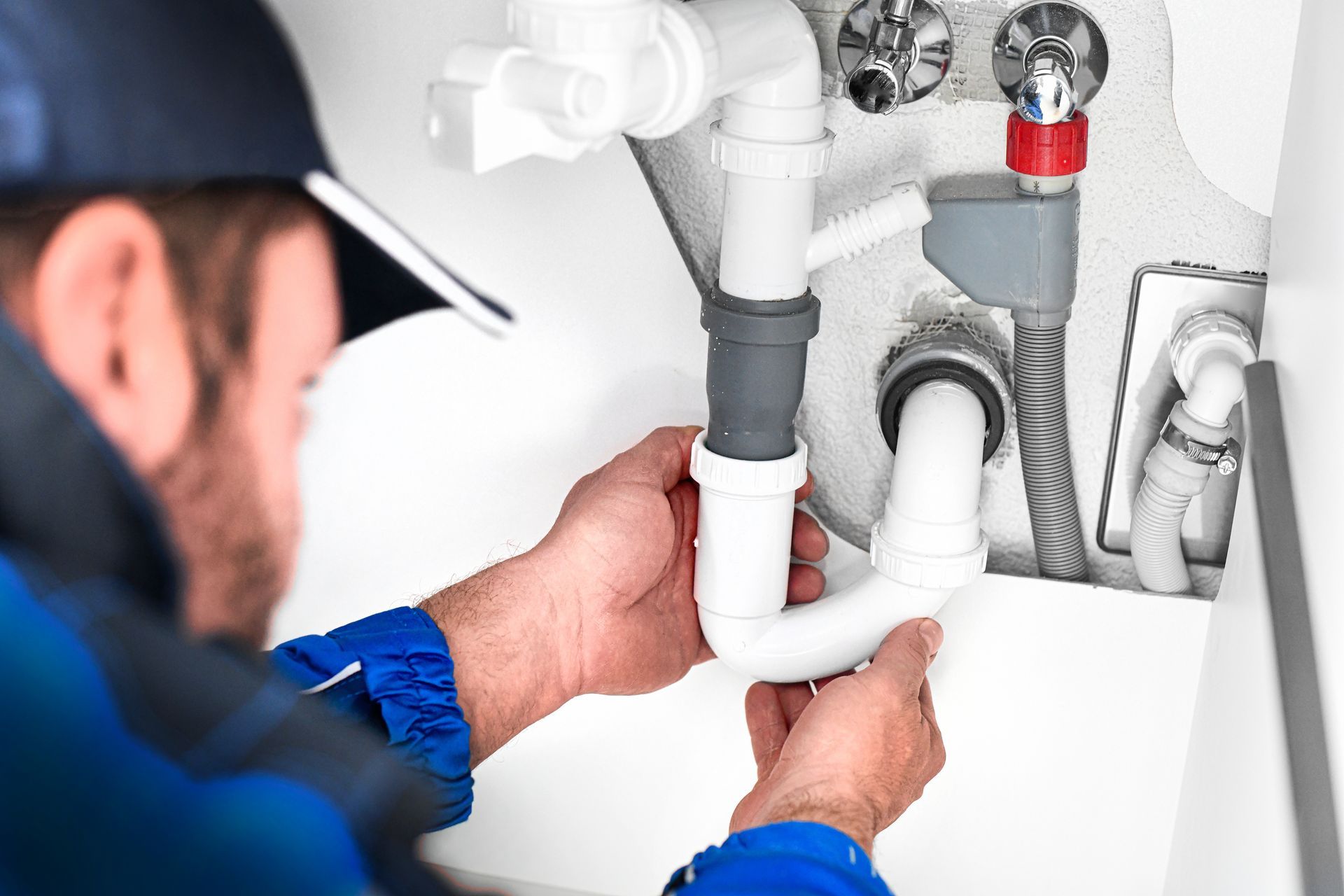 Plumber connecting white PVC pipes under a sink with tools in a kitchen cabinet