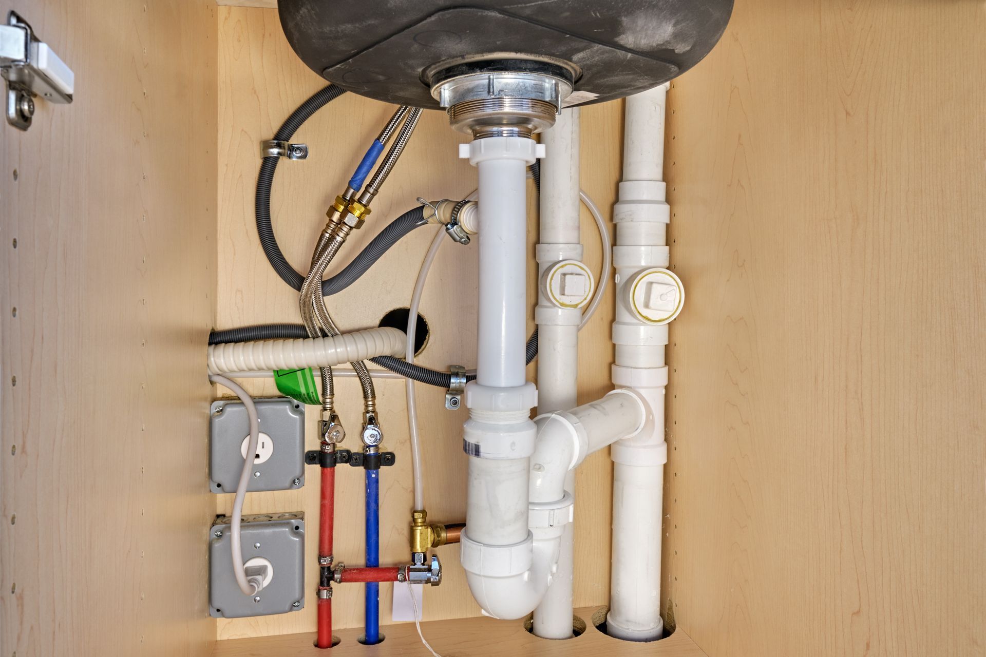 Under-sink plumbing with pipes, valves, and drain fittings inside a cabinet